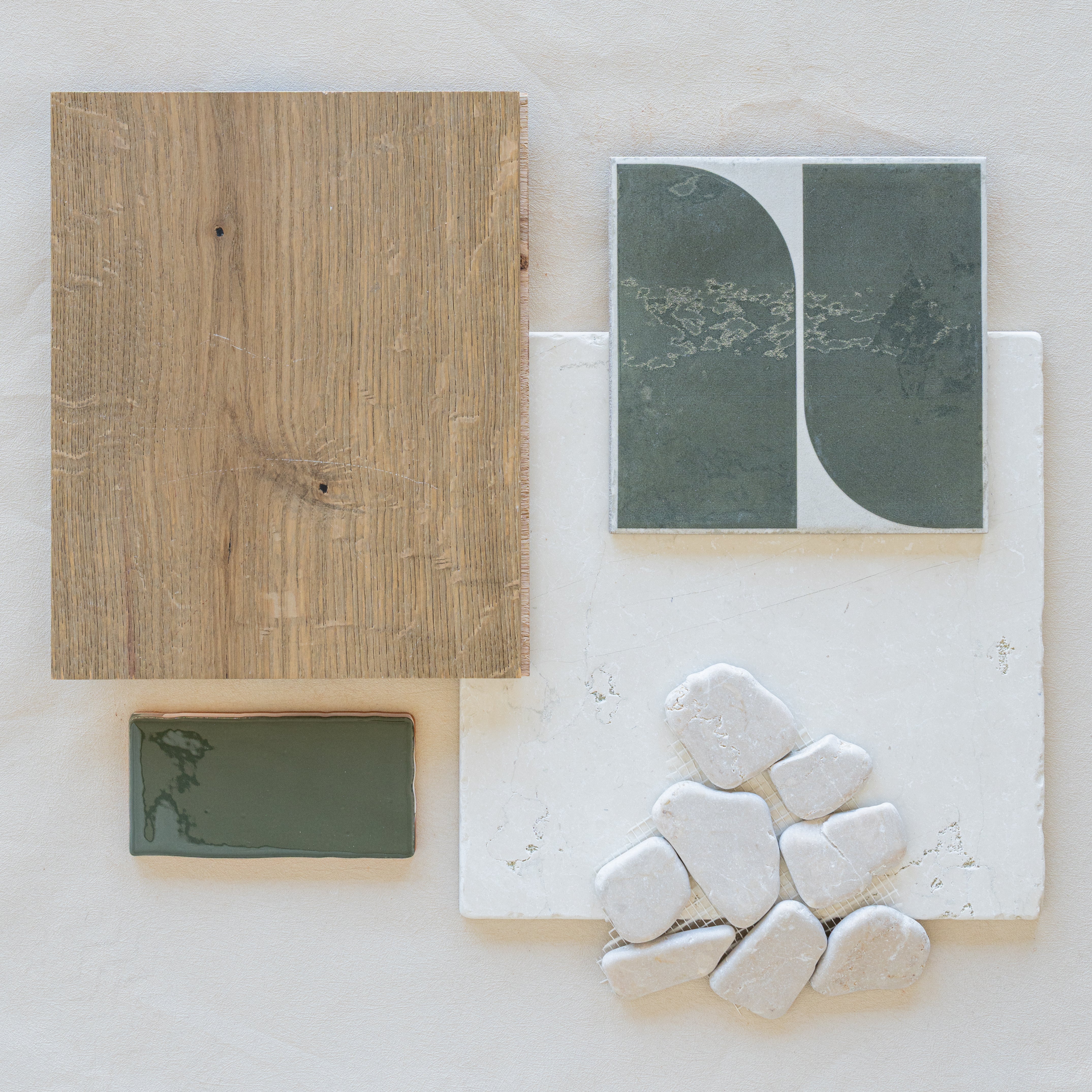 Flat lay of natural wood, green ceramic tiles, white textured tile, and smooth pale stones on a neutral surface