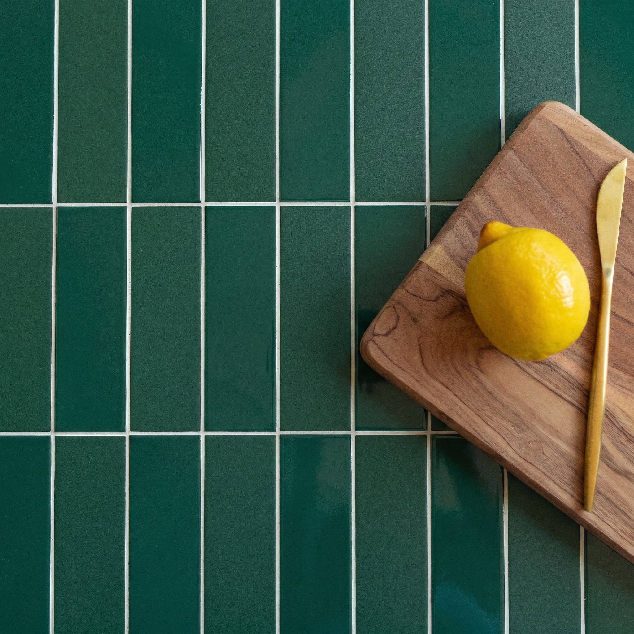 Dark green rectangular ceramic tiles with white grout next to a wooden cutting board holding a lemon and gold-toned knife