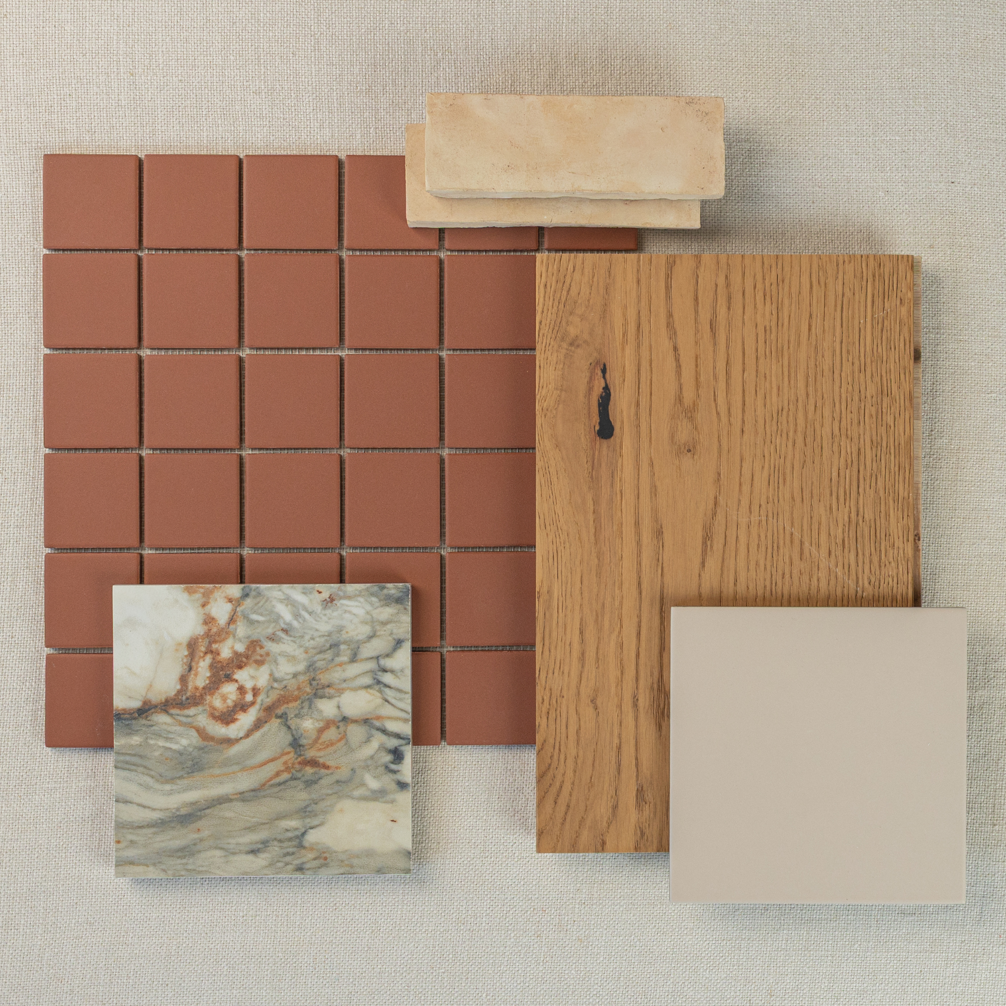 Flat lay of terracotta mosaic tiles, natural oak wood sample, beige square tile, marbled stone tile, and light beige brick accents on neutral fabric