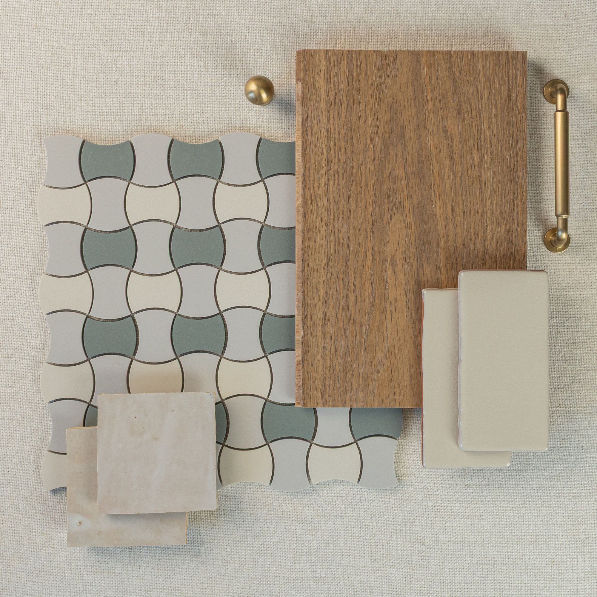 Flat lay of curved patterned ceramic tiles, natural oak wood sample, beige ceramic tiles, and brass hardware on textured fabric