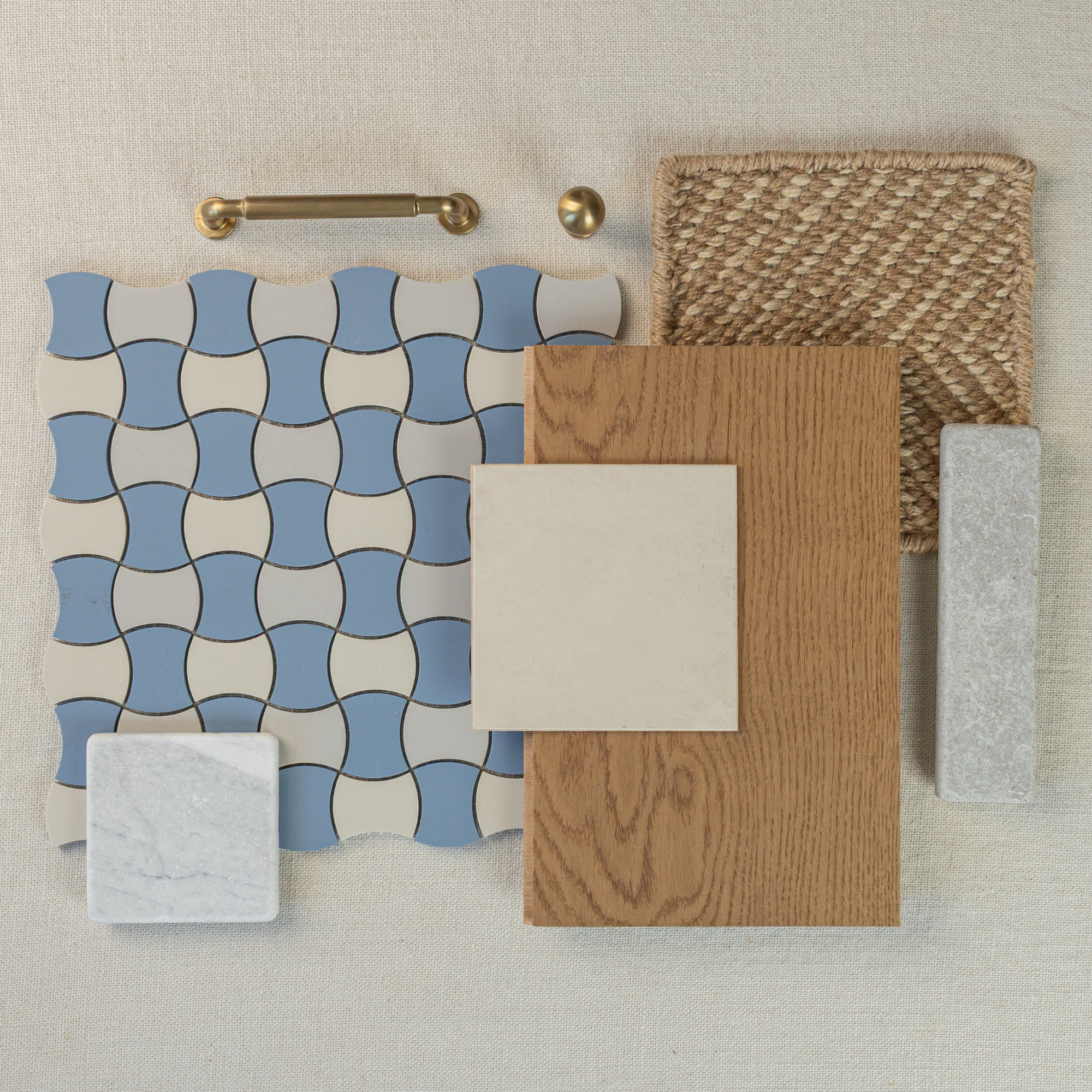 Flat lay of blue and cream curved ceramic tiles, oak wood sample, beige tile, textured woven mat, and brass cabinet hardware