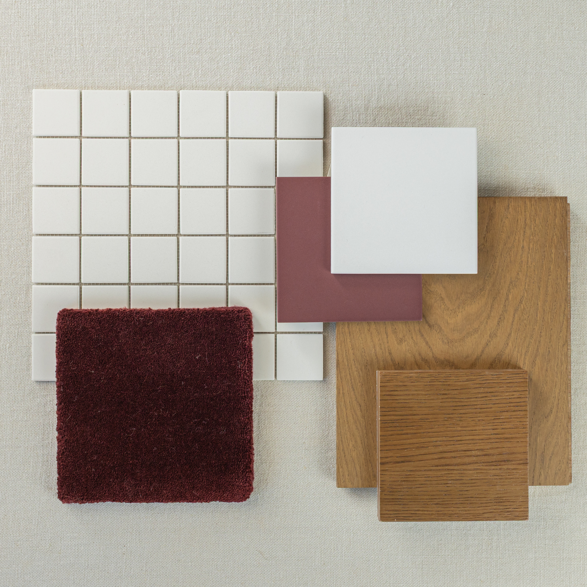 Flat lay of white ceramic tiles, deep red fabric, muted red tile, and two wood samples on textured neutral fabric