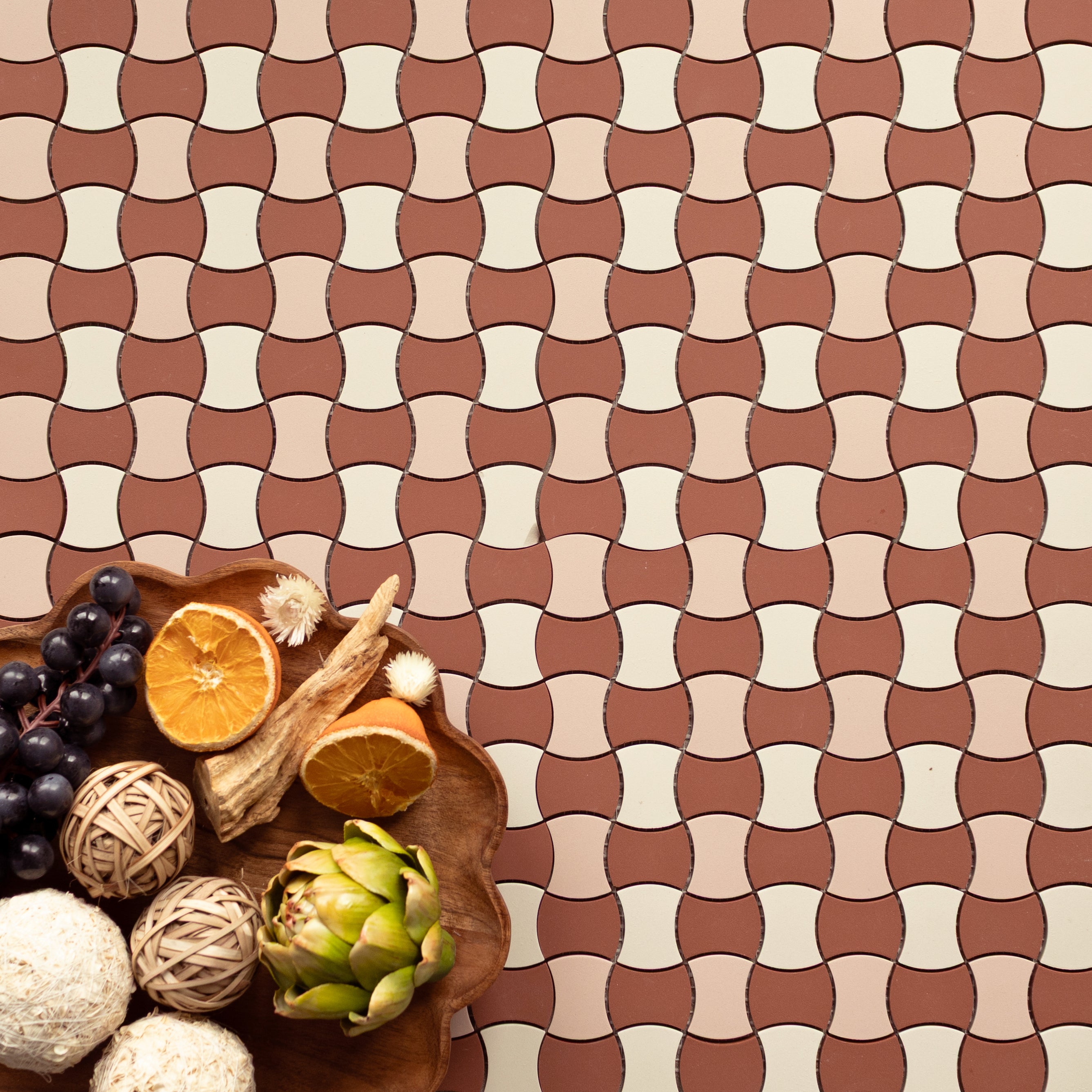 Flat lay of curved geometric terracotta and cream tiles with a wooden bowl holding fruit, dried florals, and natural decor items