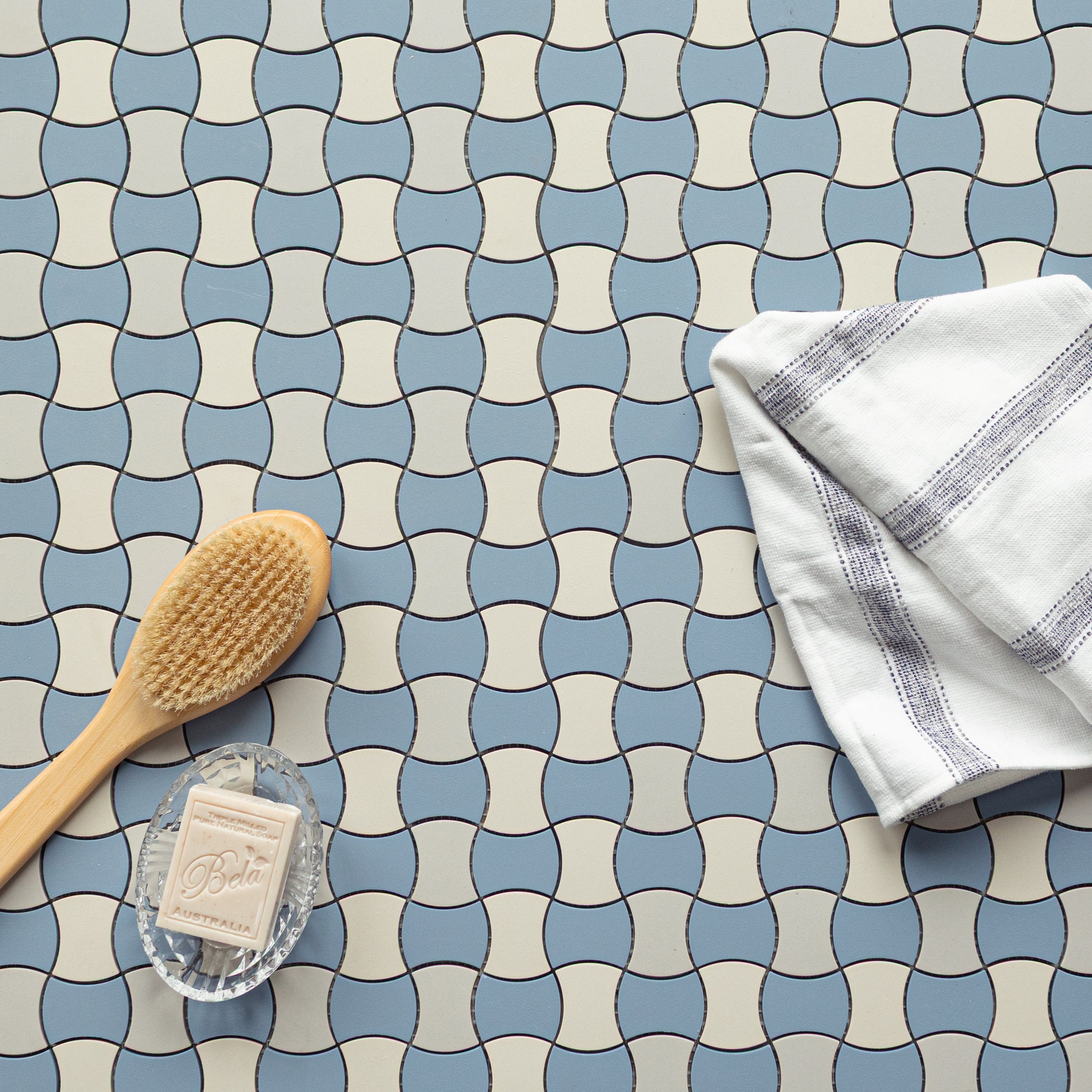 Blue and beige interlocking ceramic tiles with a wooden brush, soap bar, and folded white cloth on top