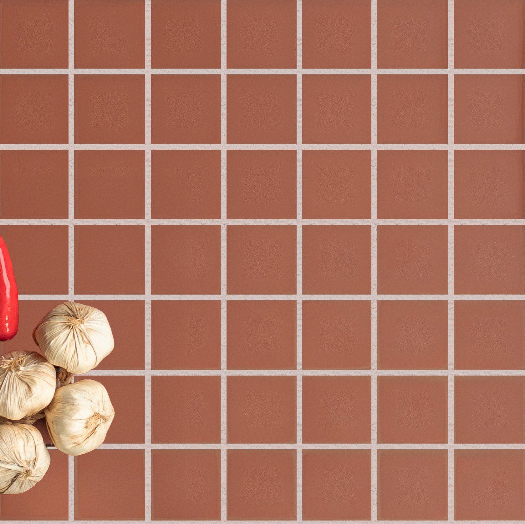 Square terracotta ceramic tiles with light grout lines and garlic bulbs resting in the corner on the tiled surface