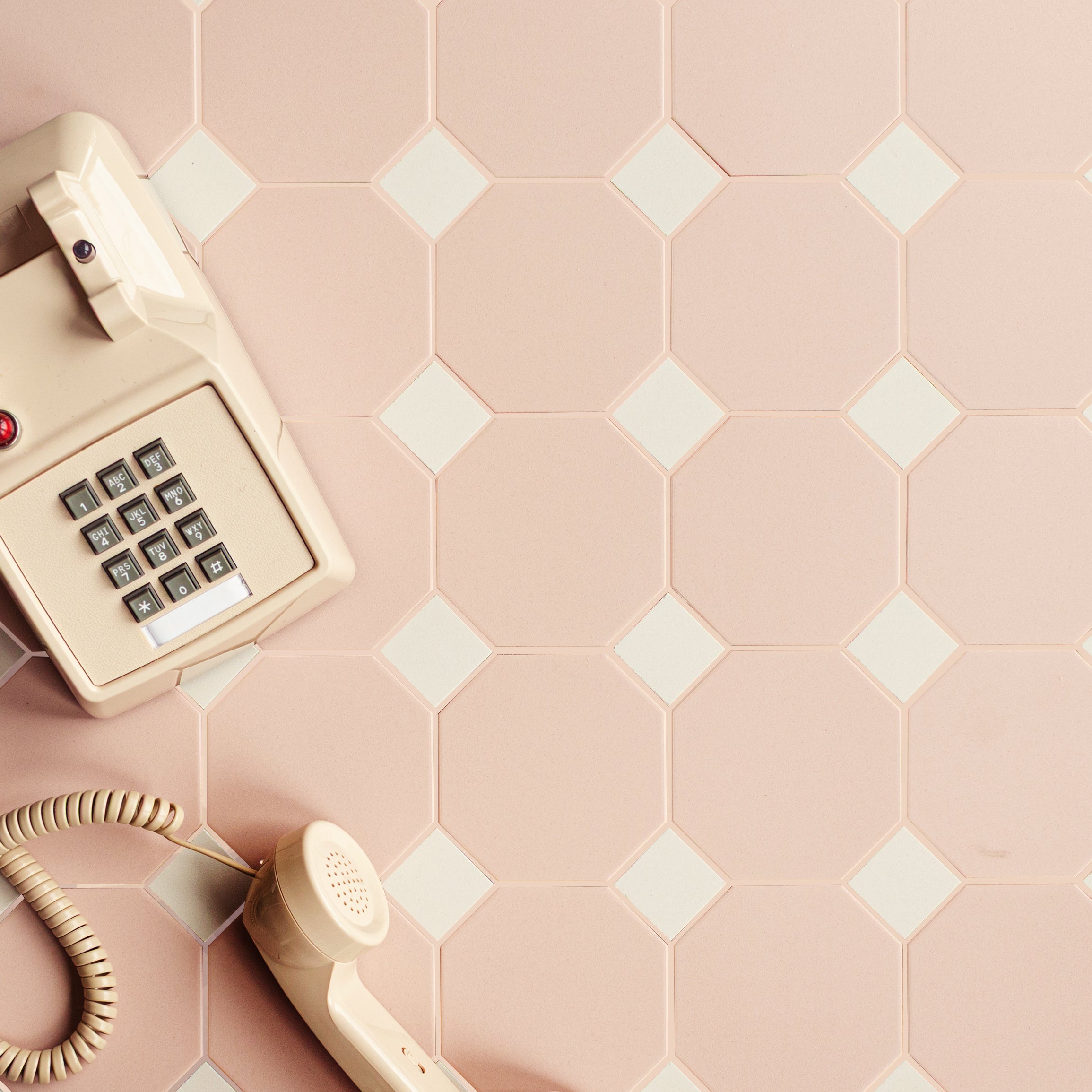 Vintage beige wall-mounted phone with cord resting on geometric ceramic tiles in soft pink and white tones
