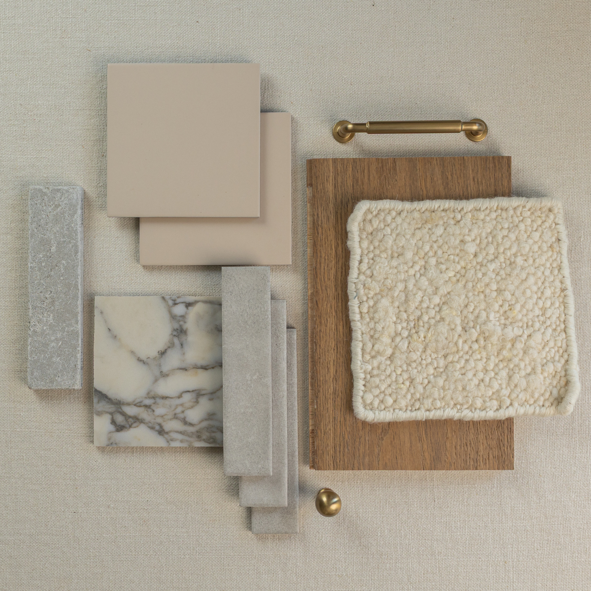 Flat lay of neutral beige ceramic tiles, gray stone samples, marble tile, wood swatch, textured fabric, and gold hardware on linen background