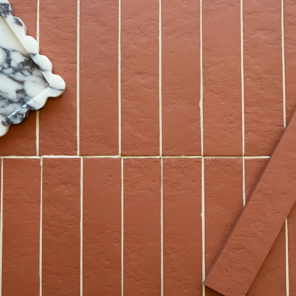 Rustic terracotta tiles arranged in vertical rows with white grout lines alongside a marble tray corner and matching tile sample.