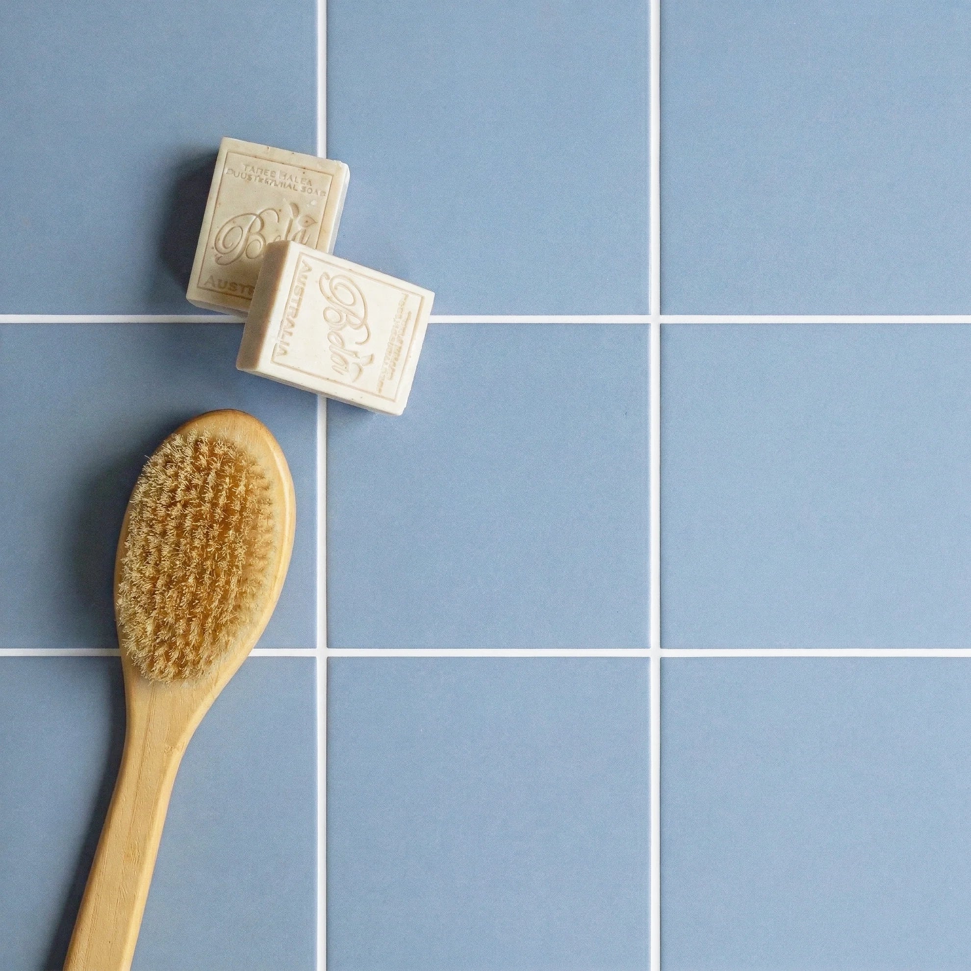Blue square ceramic tiles with visible white grout, accompanied by a wooden bath brush and two bars of soap