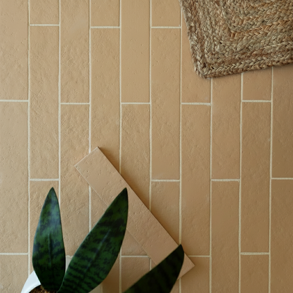 Soft beige ceramic tiles arranged in a staggered rectangular pattern with green plant leaves and woven mat corner