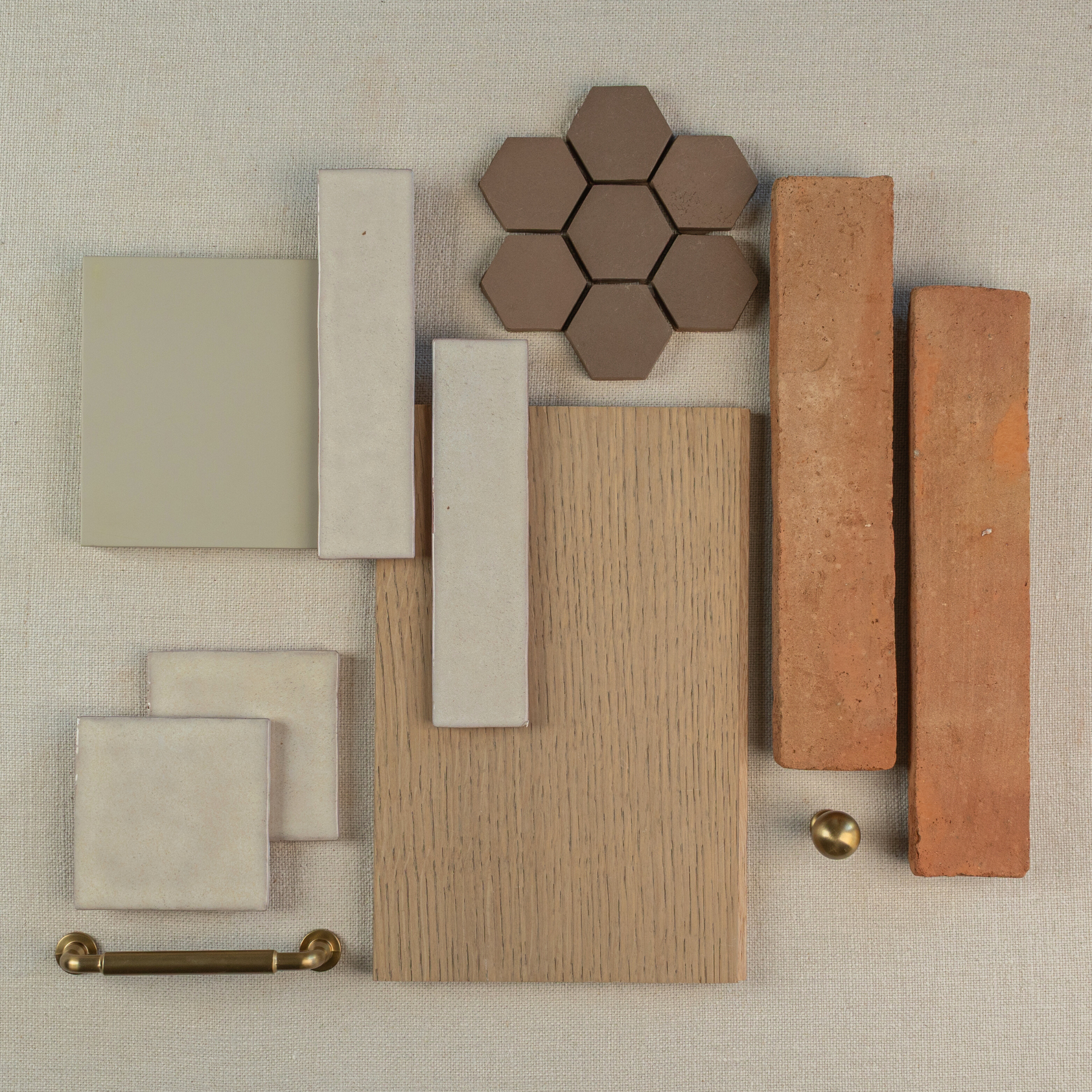Assorted building materials including hexagonal brown tiles, wood plank, terracotta bricks, beige tiles, and brass hardware on fabric background