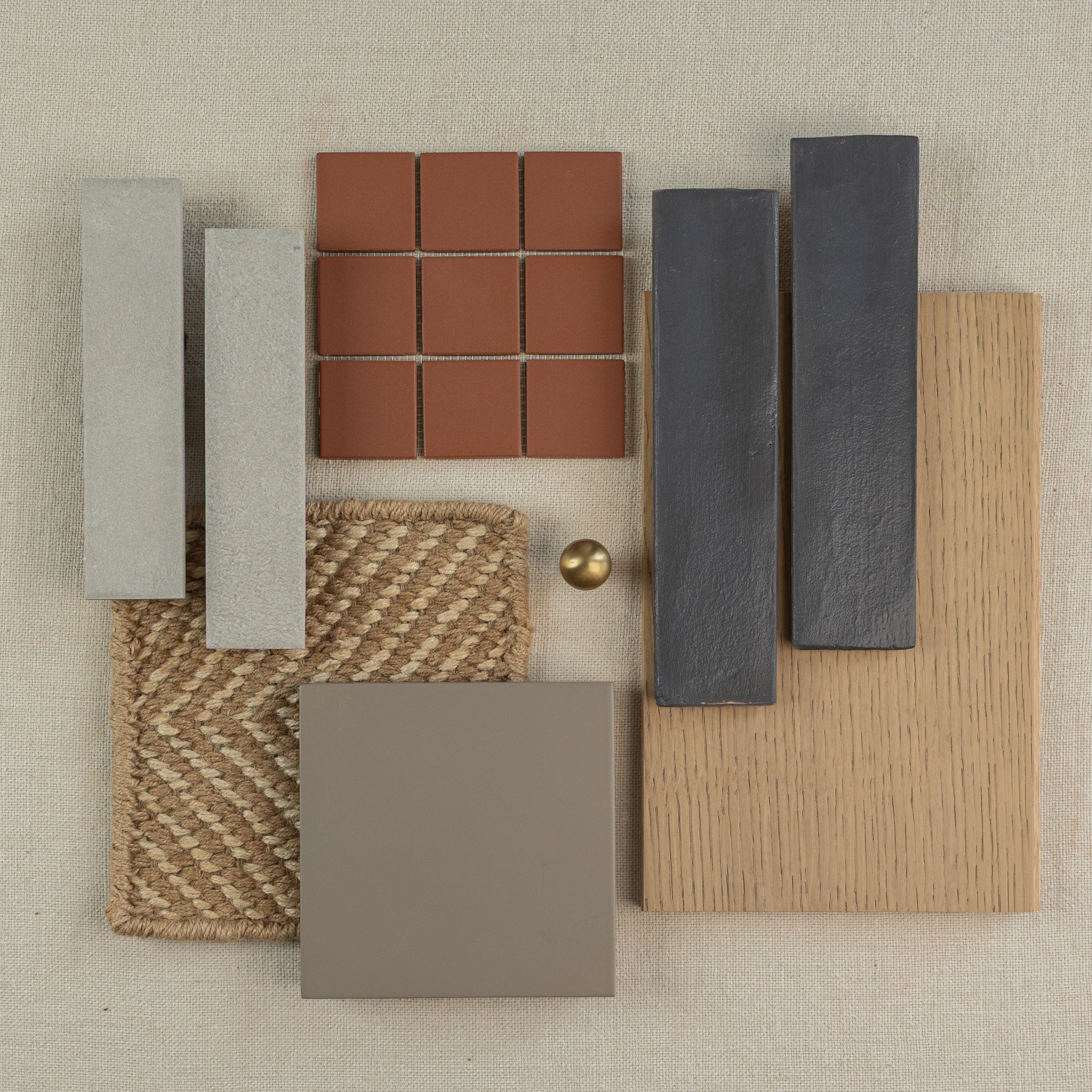 Collection of handmade terracotta tiles with wood, stone, fabric samples, and a brass knob on a neutral background