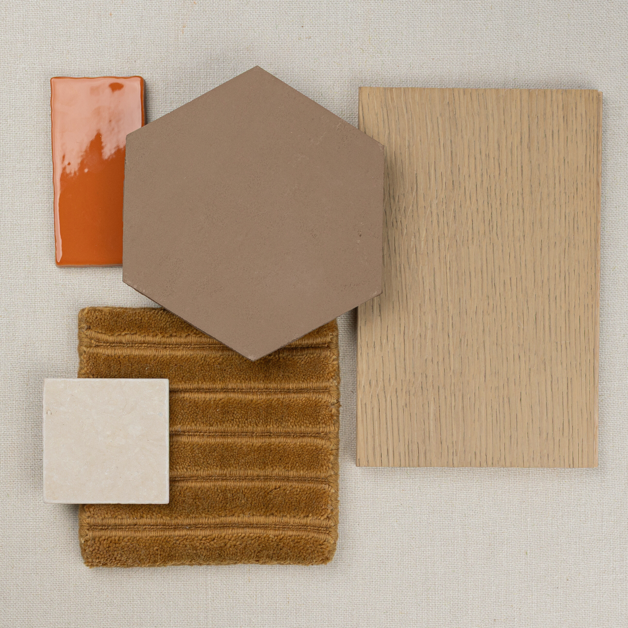 Flat lay of oak wood sample, brown hexagonal tile, burnt orange ceramic tile, beige square tile, and textured golden fabric on neutral background