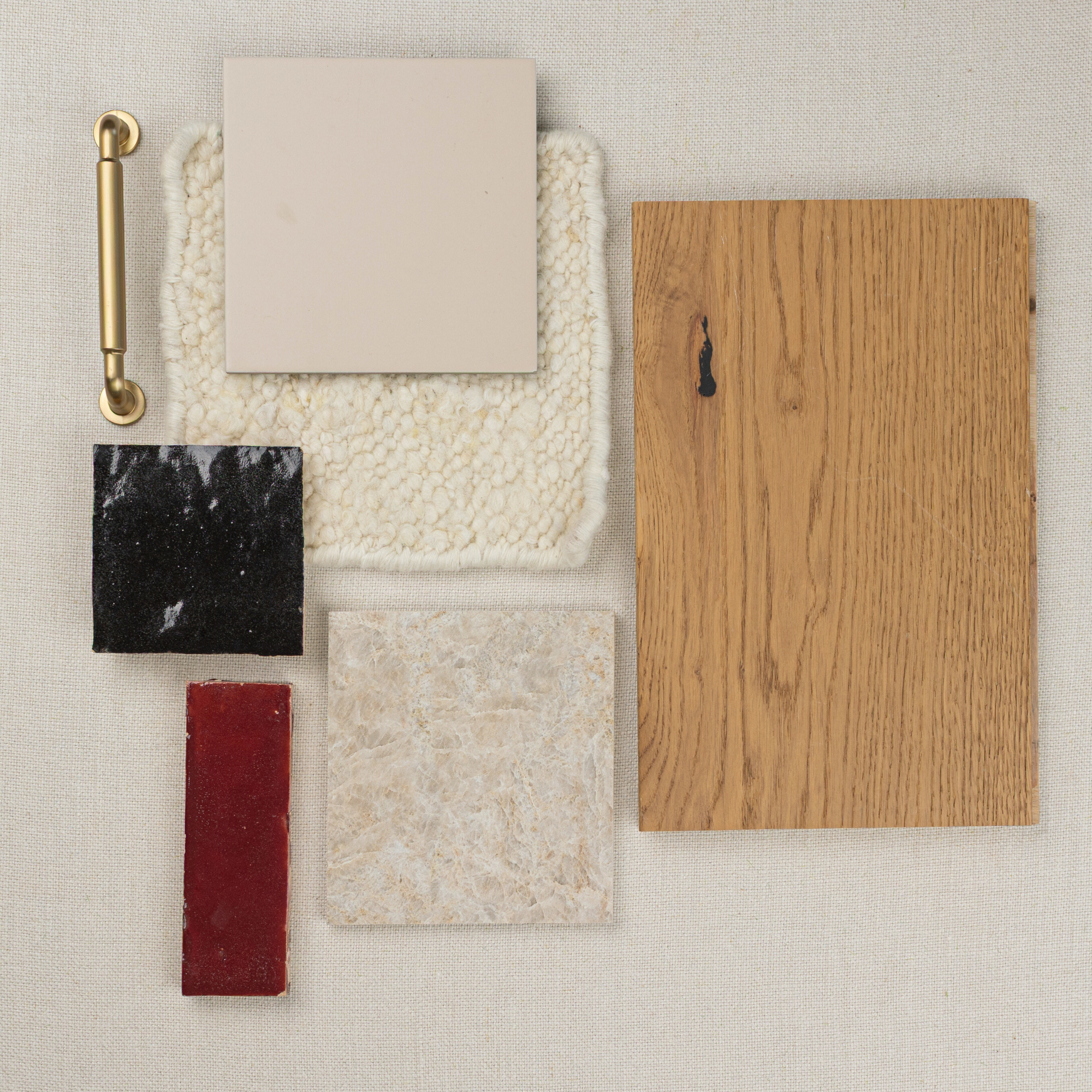 Overhead view of oak wood sample, creamy tile, red and black ceramic pieces, textured fabric, and brass handle on neutral background