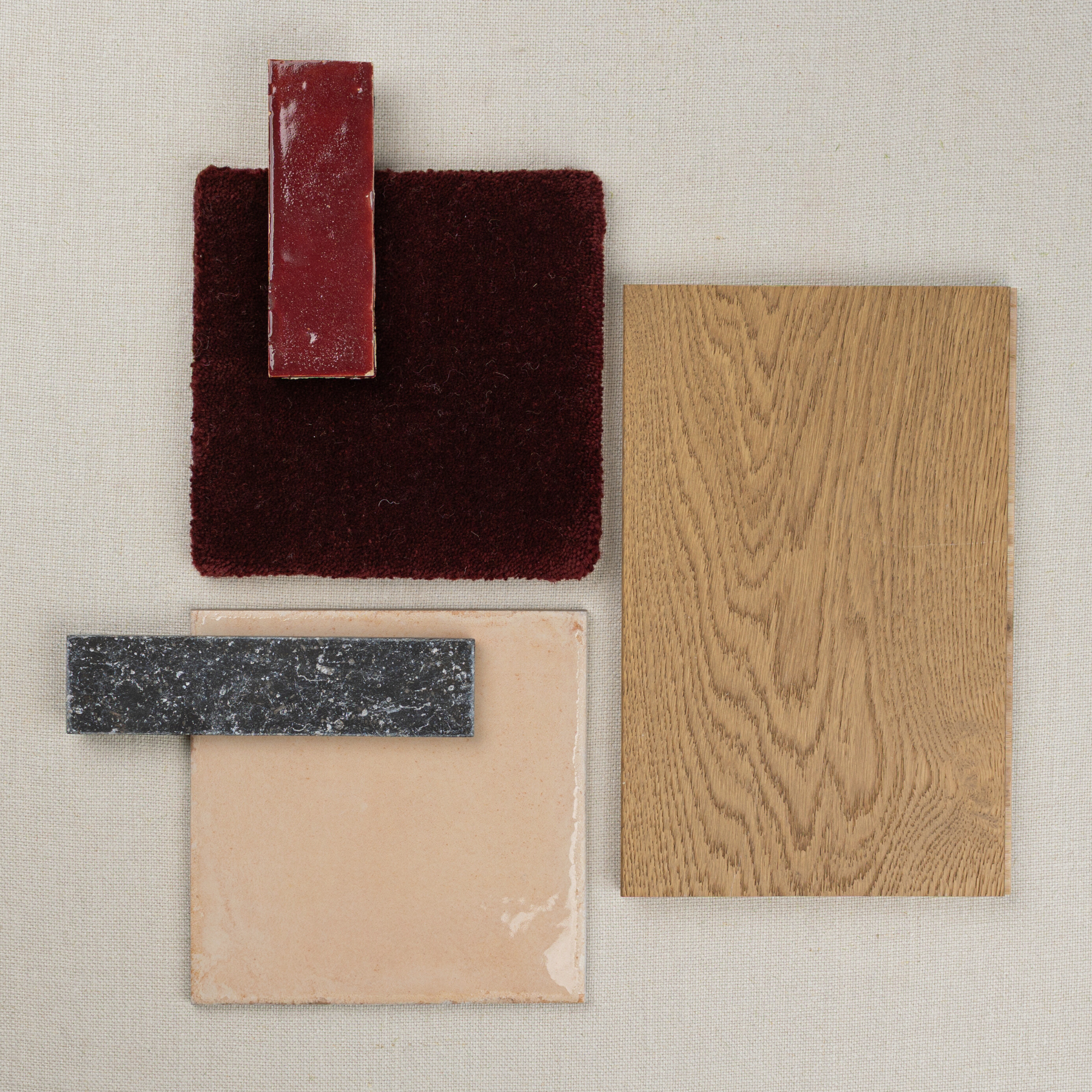 Flat lay of oak wood sample with red terracotta tile, deep burgundy fabric swatch, beige ceramic tile, and dark gray stone strip on neutral background