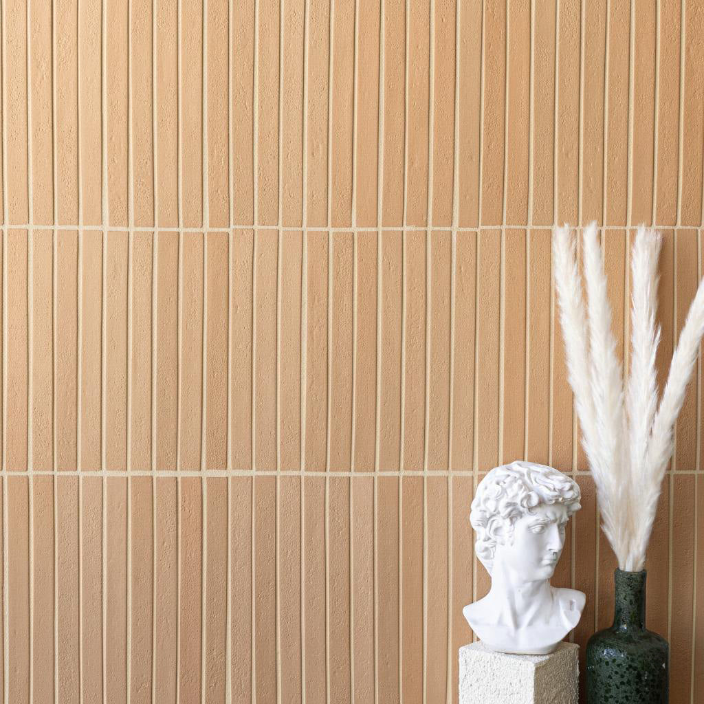 Vertical narrow terracotta tiles with light grout behind a white classical bust and tall dried pampas grass in a green vase