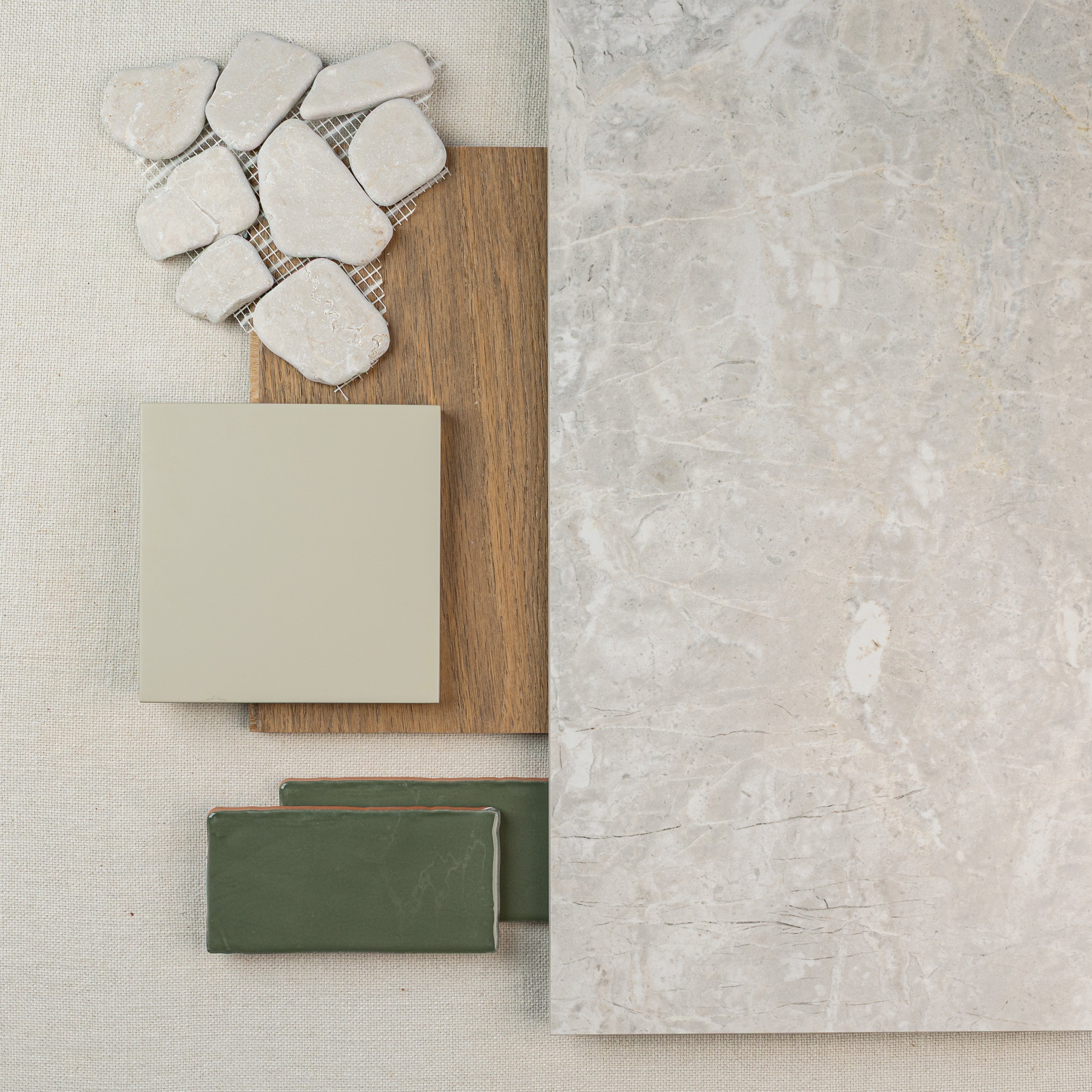 Neutral stone mosaic pieces, pale beige tile, wood plank sample, green ceramic tiles, and large light gray marble slab arranged on fabric.