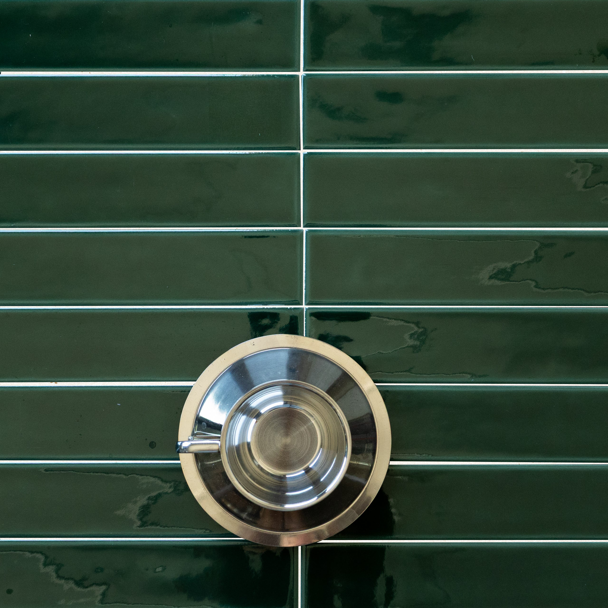 Glossy deep green rectangular ceramic tiles with thin grout lines and a reflective silver metal ring placed on top