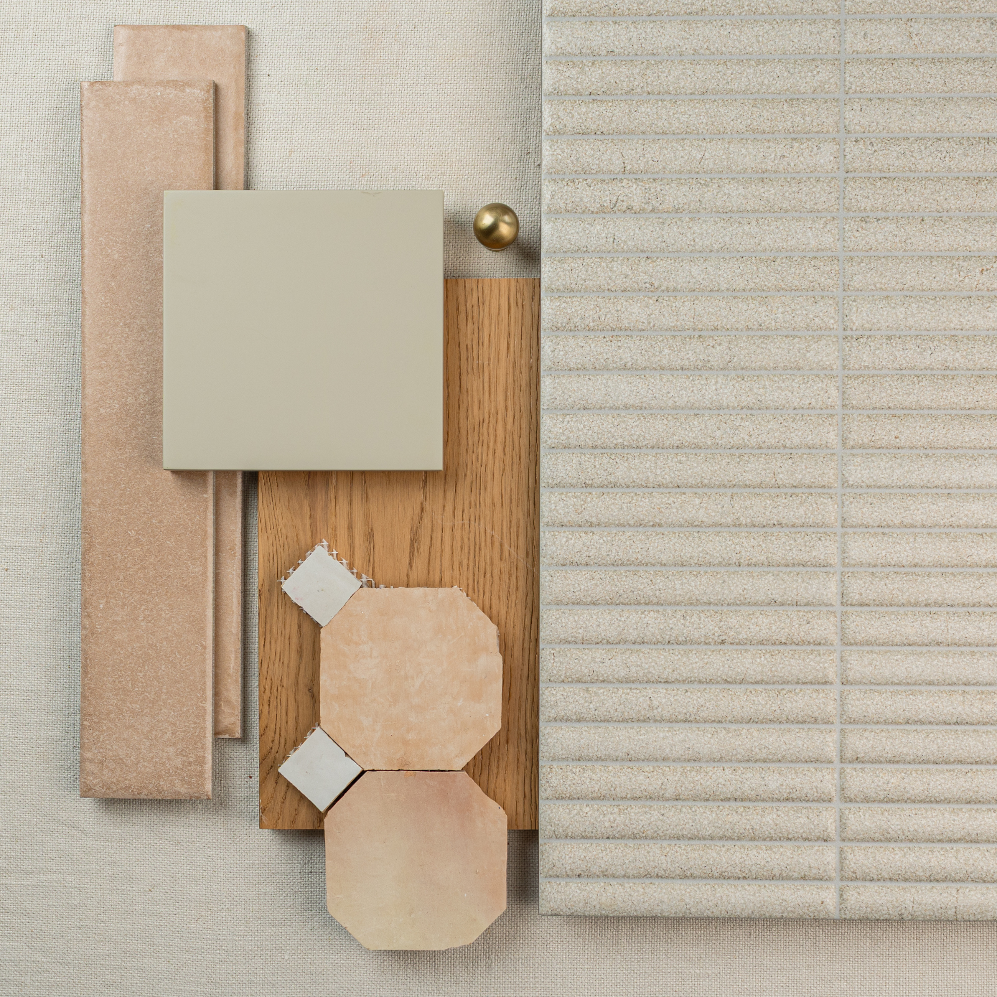 Flat lay of beige and cream textured tiles, wood plank sample, octagonal tile pieces, and a brass accent on neutral fabric