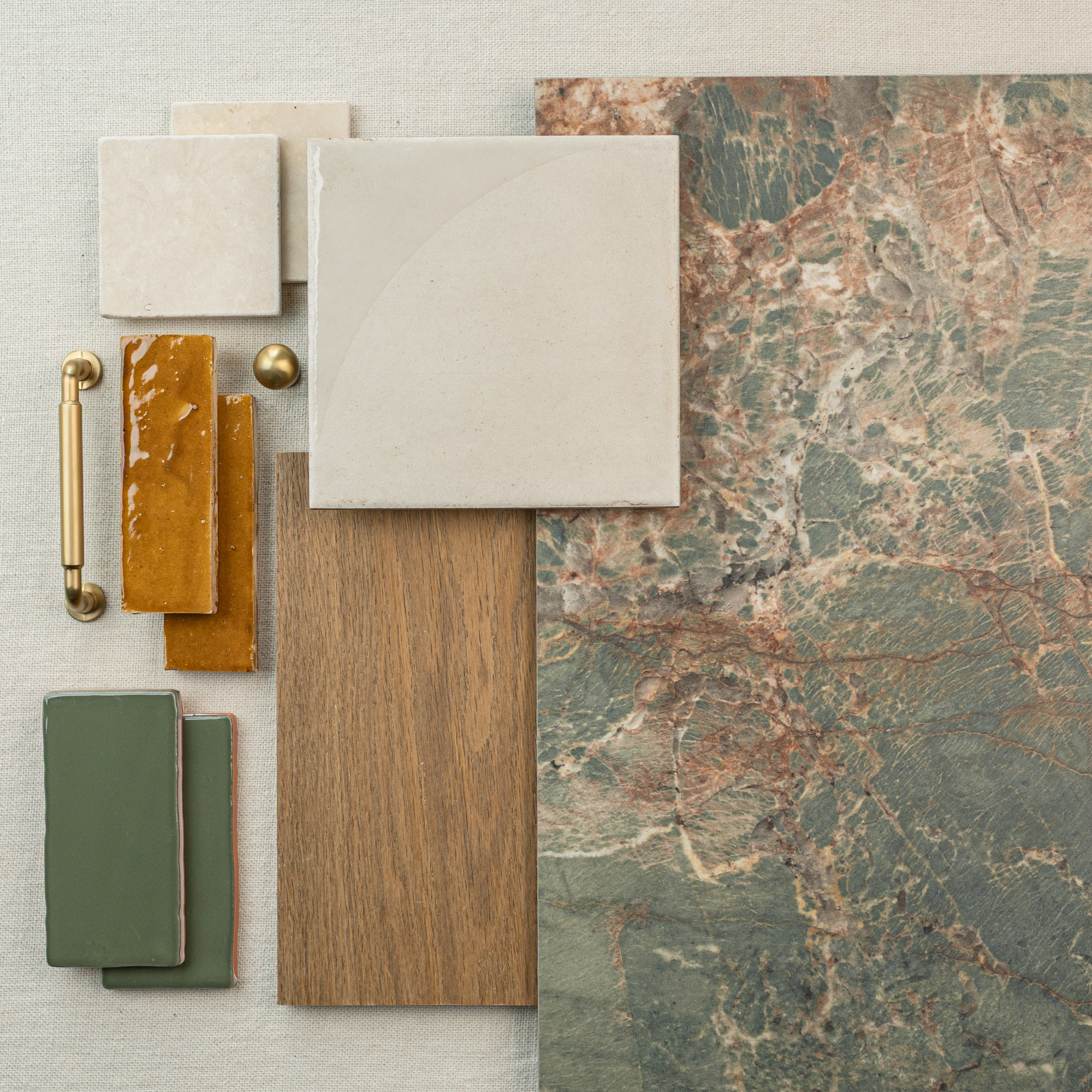 Flat lay of large green and rust marble tile with wood plank, beige ceramic tiles, green tiles, and brass hardware on fabric background