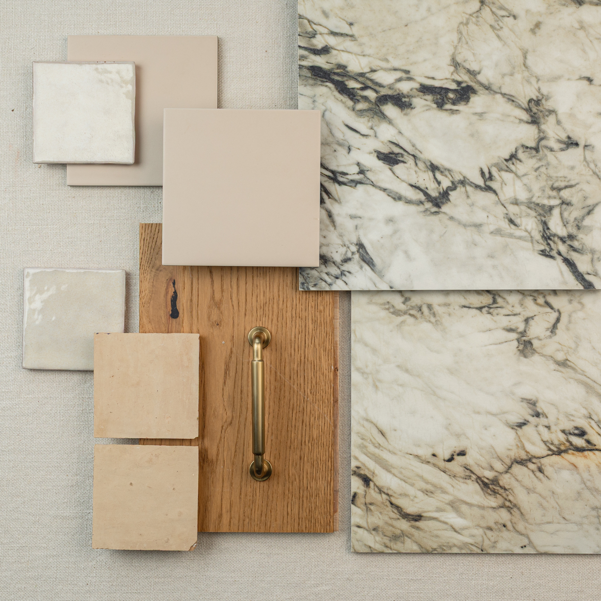 Assortment of large format marble-effect tiles, beige ceramic samples, and wood panel with brass handle on fabric background