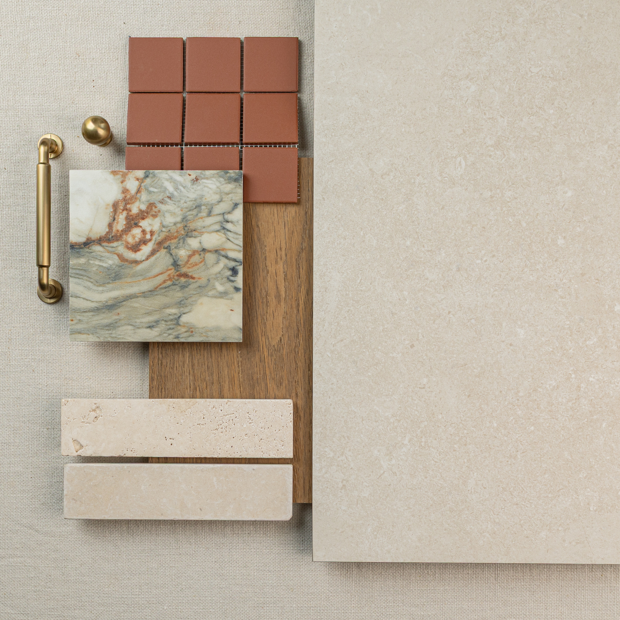 Flat lay of cream large format tile, wood plank, terracotta ceramic tiles, marble tile, brass handle, and limestone samples on fabric