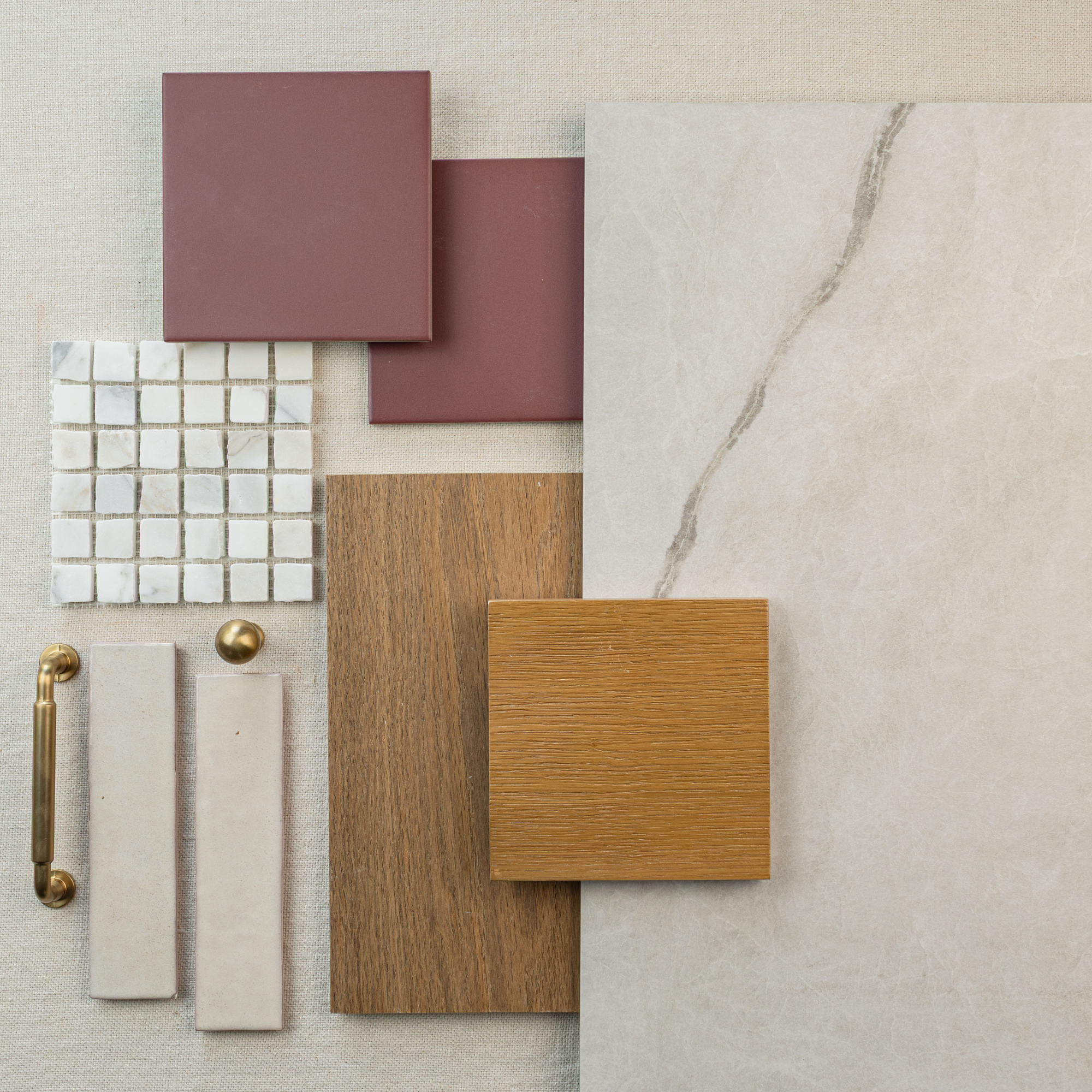 Overhead view of beige marble-look tile, oak wood sample, mauve square tiles, white mosaic tiles, and brass hardware pieces