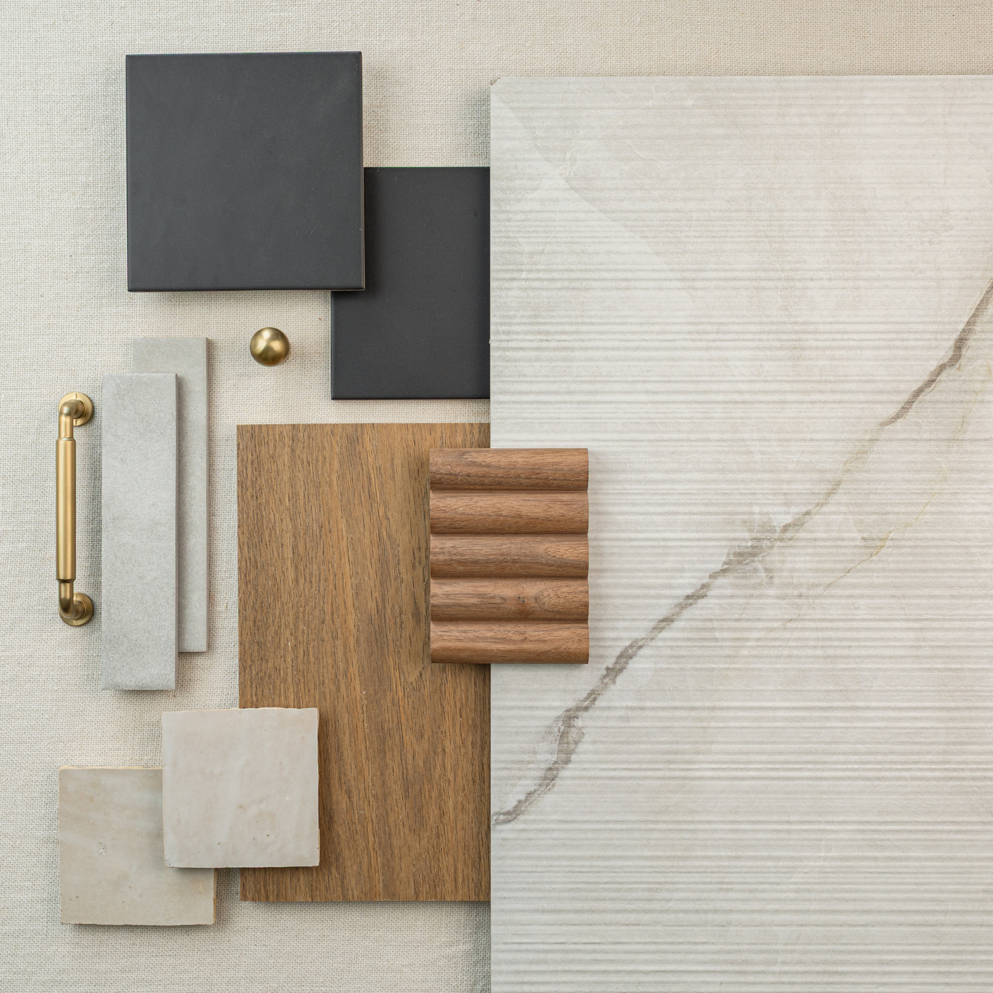 Flat lay of textured cream large format tile with wood samples, matte black tiles, brass hardware, and beige ceramic accents