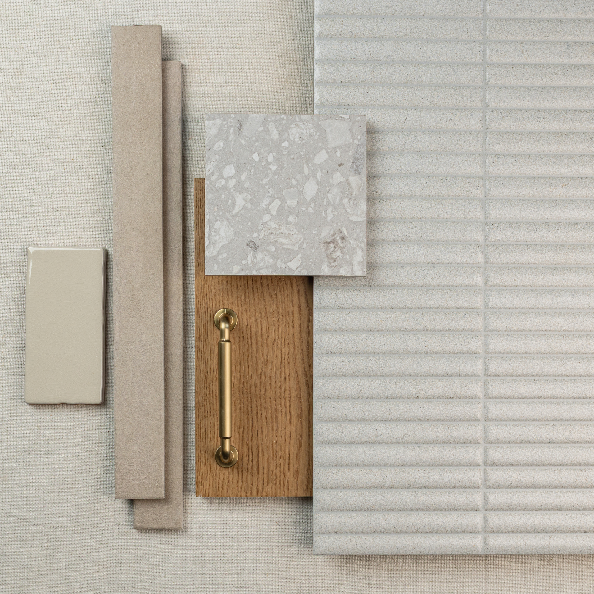 Overhead display of neutral fabric swatches with wood plank, terrazzo tile, rectangular tile, and brass handle pieces arranged neatly