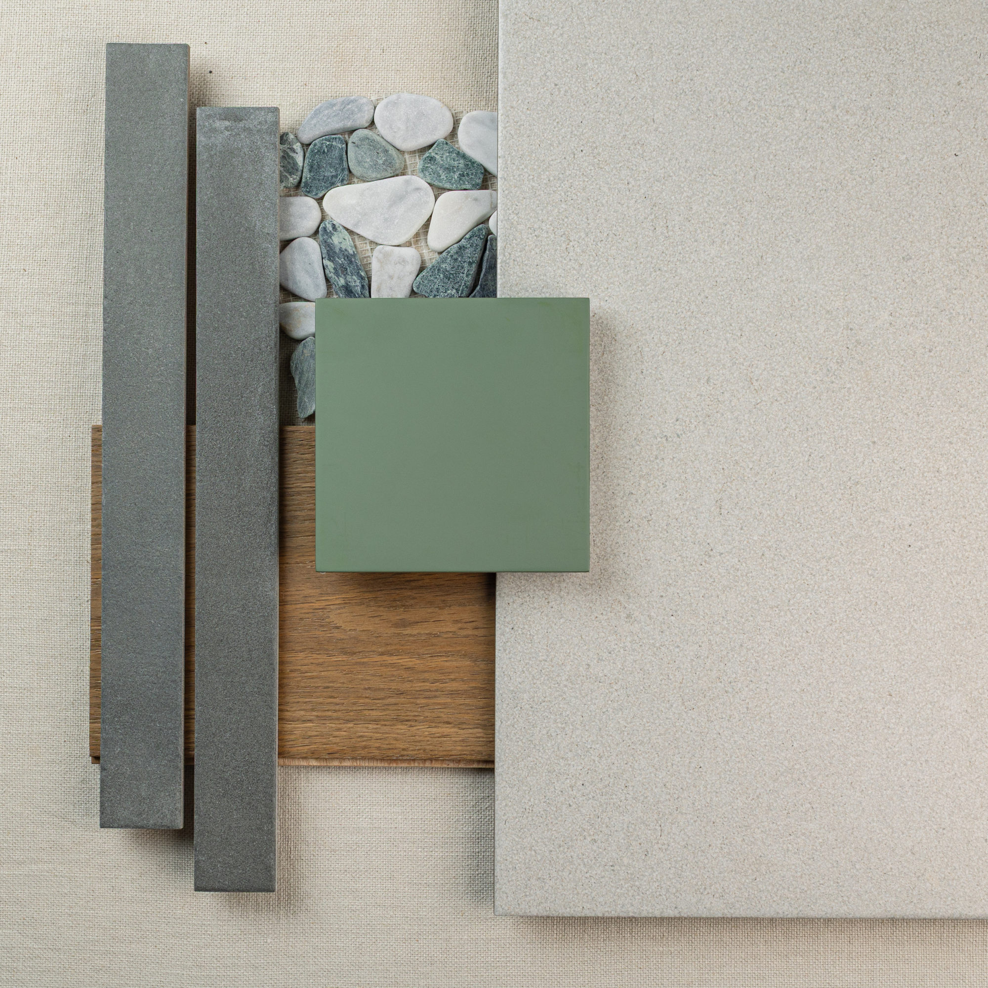 Top view of layered green ceramic tile, pebble mosaic, wood plank, dark rectangular tiles, and large limestone slab on a fabric surface