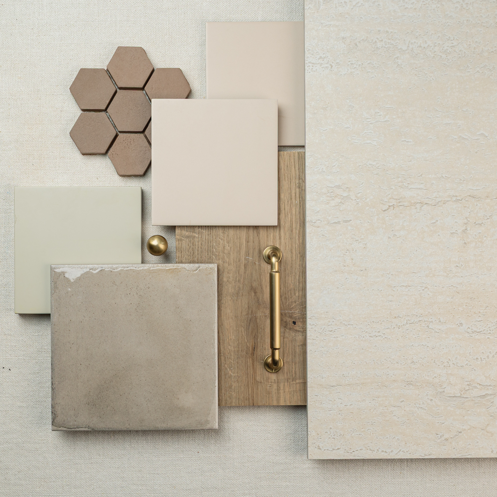 Arrangement of beige ceramic tiles, hexagonal stone tiles, wood sample, and brass hardware on a soft neutral background