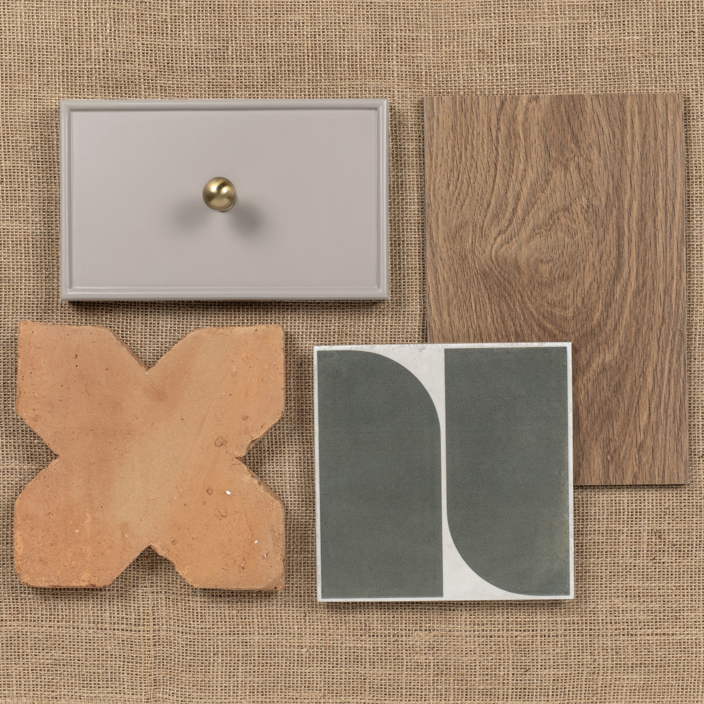 Various ceramic, terracotta, wood, and painted tile samples arranged on a burlap surface.
