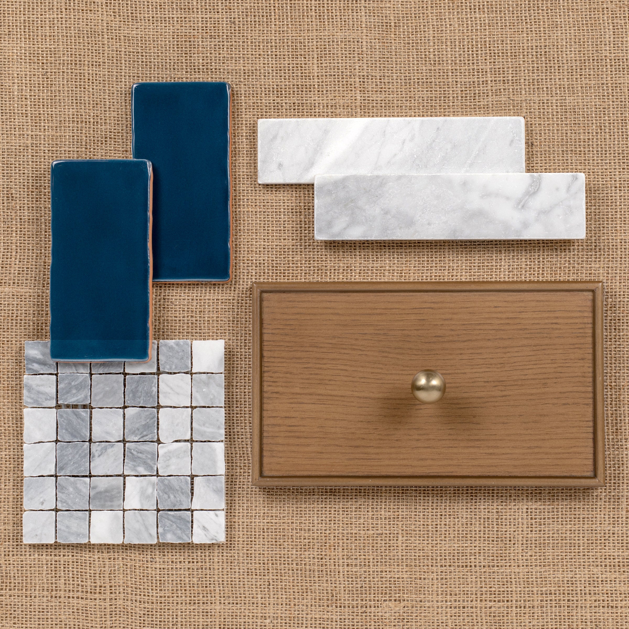 Flat lay of blue, white marble tiles and wood drawer front with brass knob on woven background