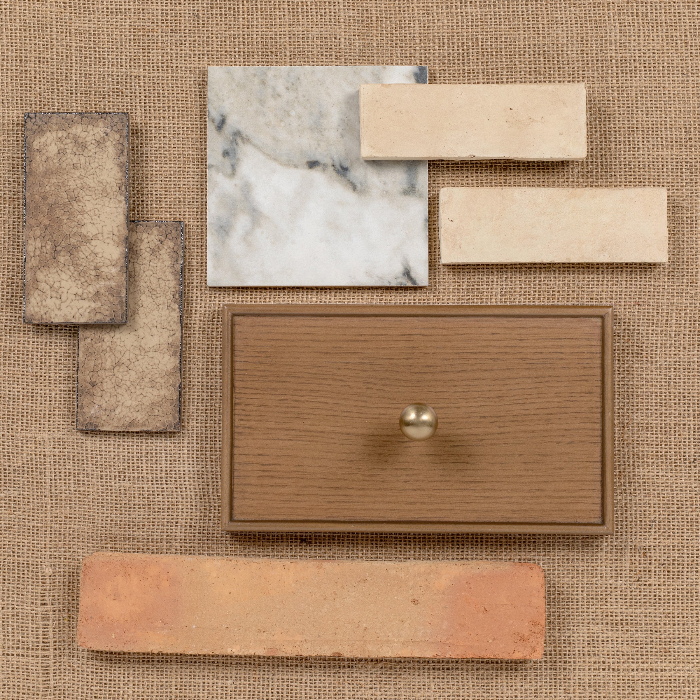 Assortment of ceramic, porcelain, and terracotta tiles with a wooden drawer front and brass knob on burlap background