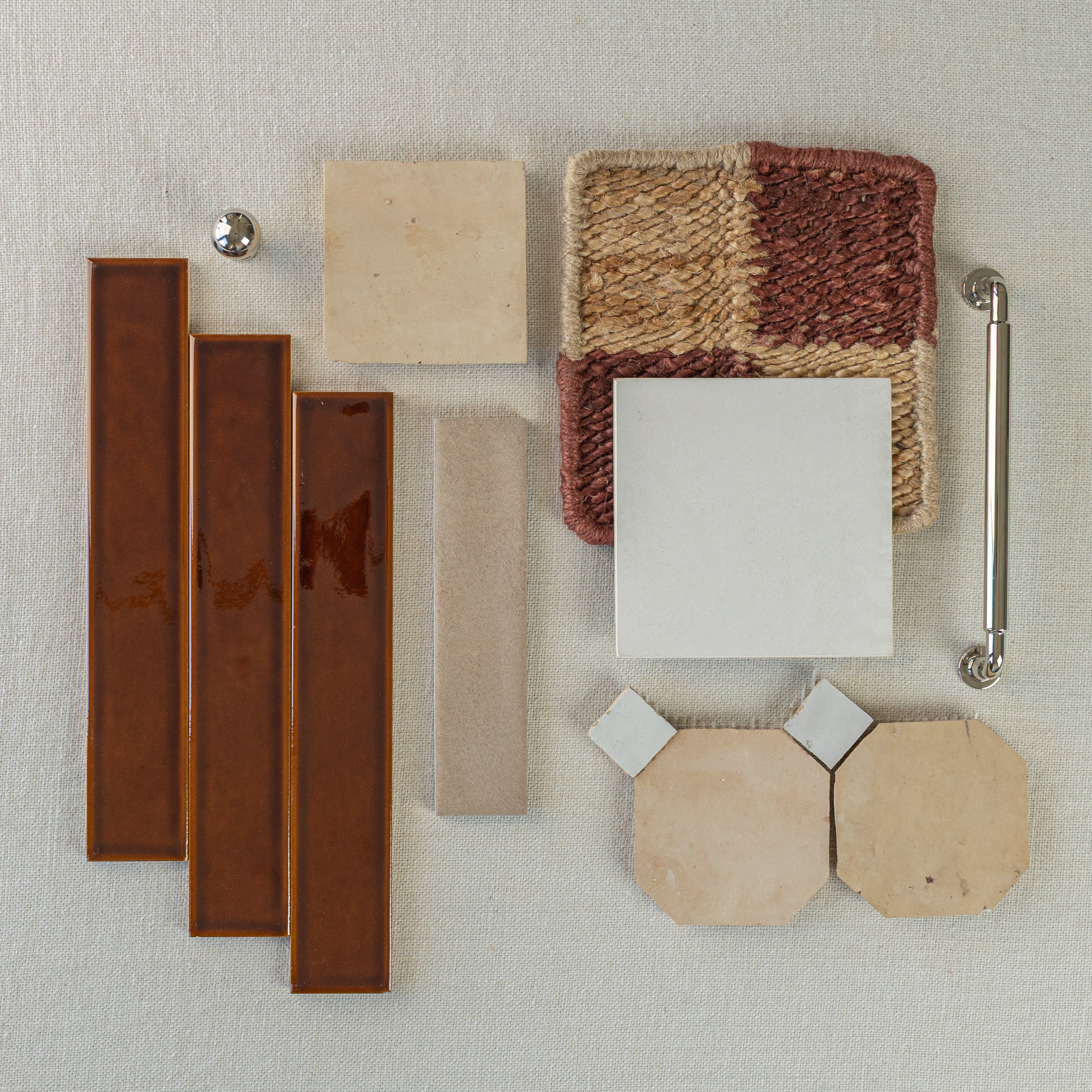 Assortment of terracotta tiles, beige ceramic squares, textured woven fabric, polished metal knob, and silver cabinet pull on fabric background