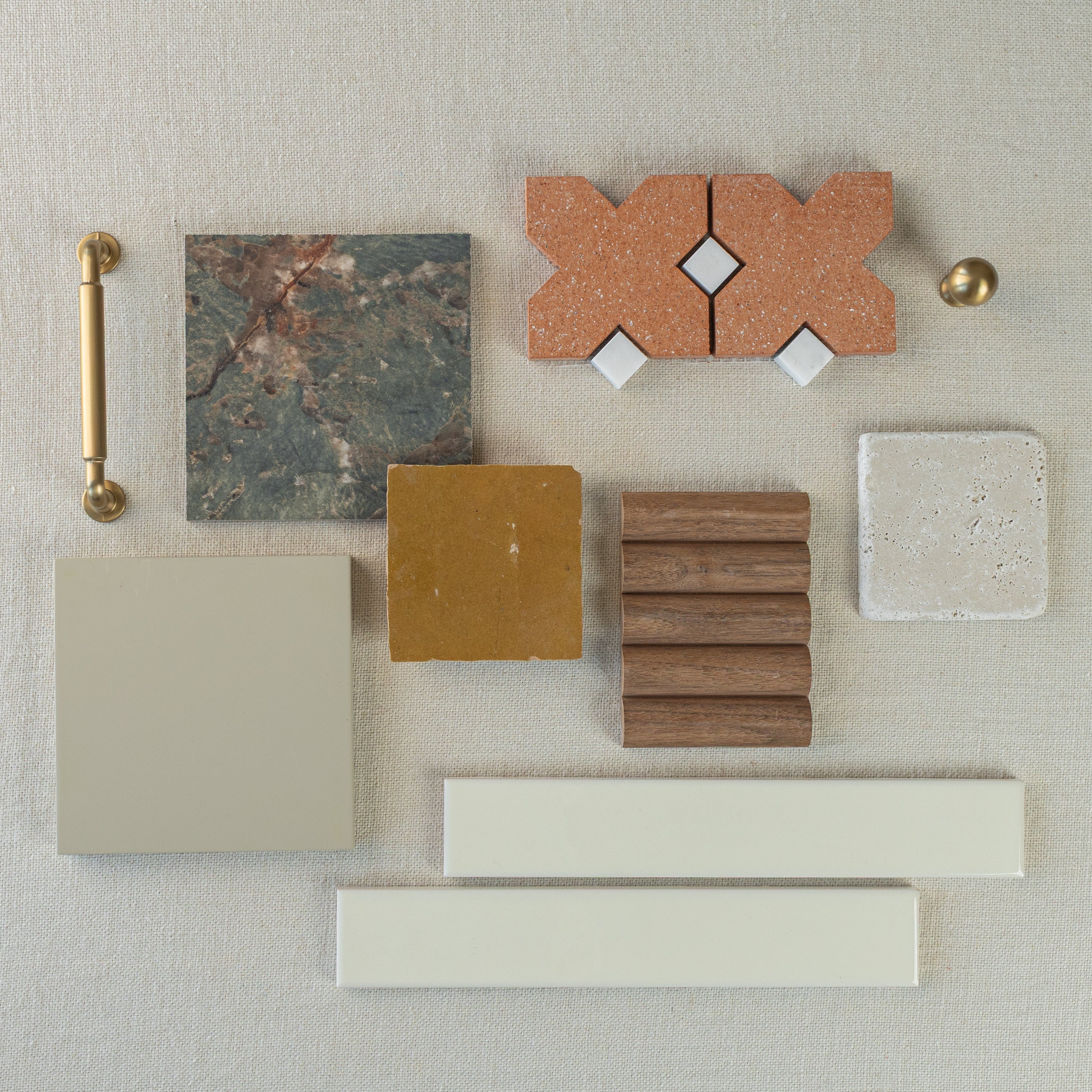 Flat lay of terracotta, beige ceramic, textured wood, gray stone, marble tile samples with brass hardware on neutral fabric background