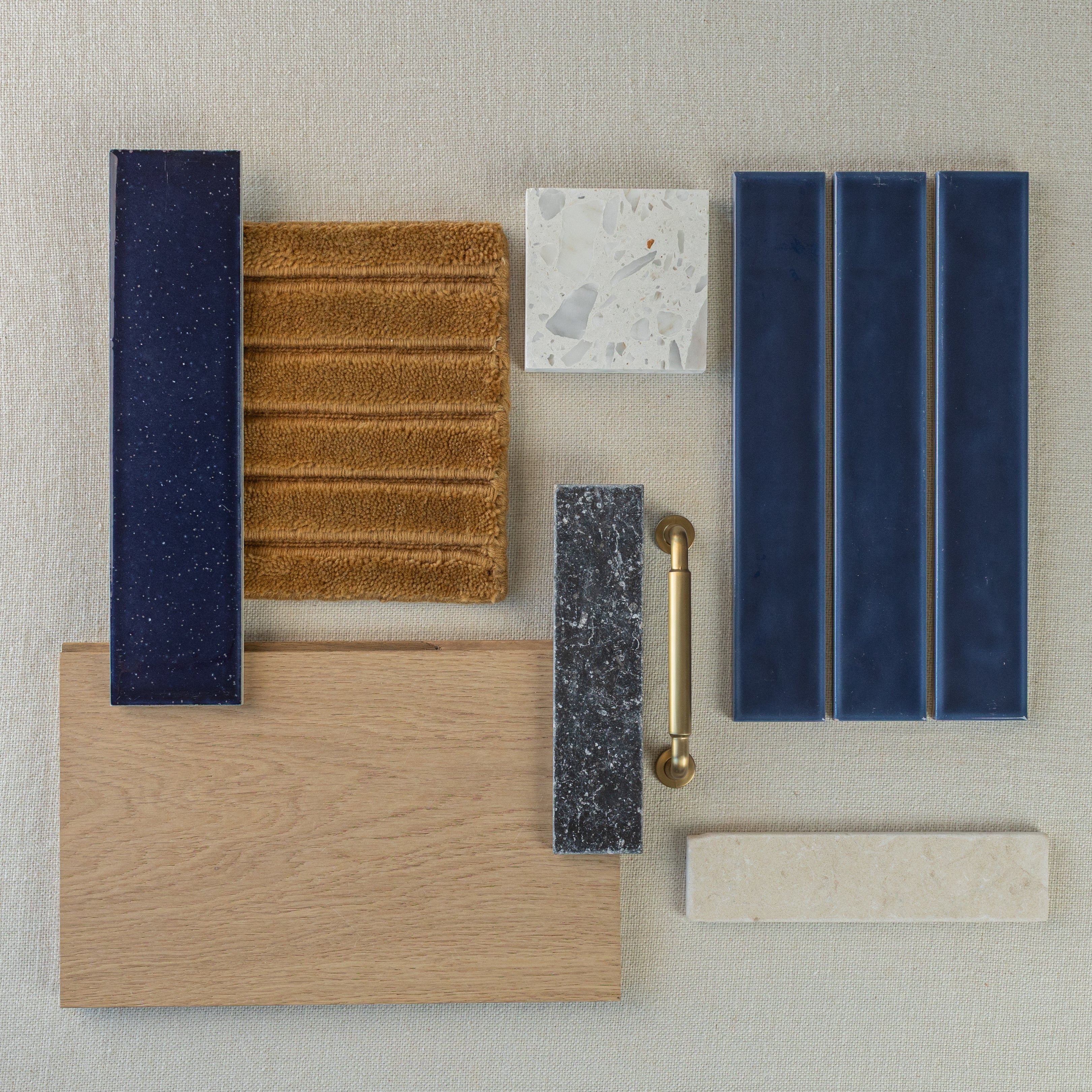 Collection of blue ceramic tiles, oak wood sample, textured brown fabric, gray stone, terrazzo, and brass cabinet handle on beige background