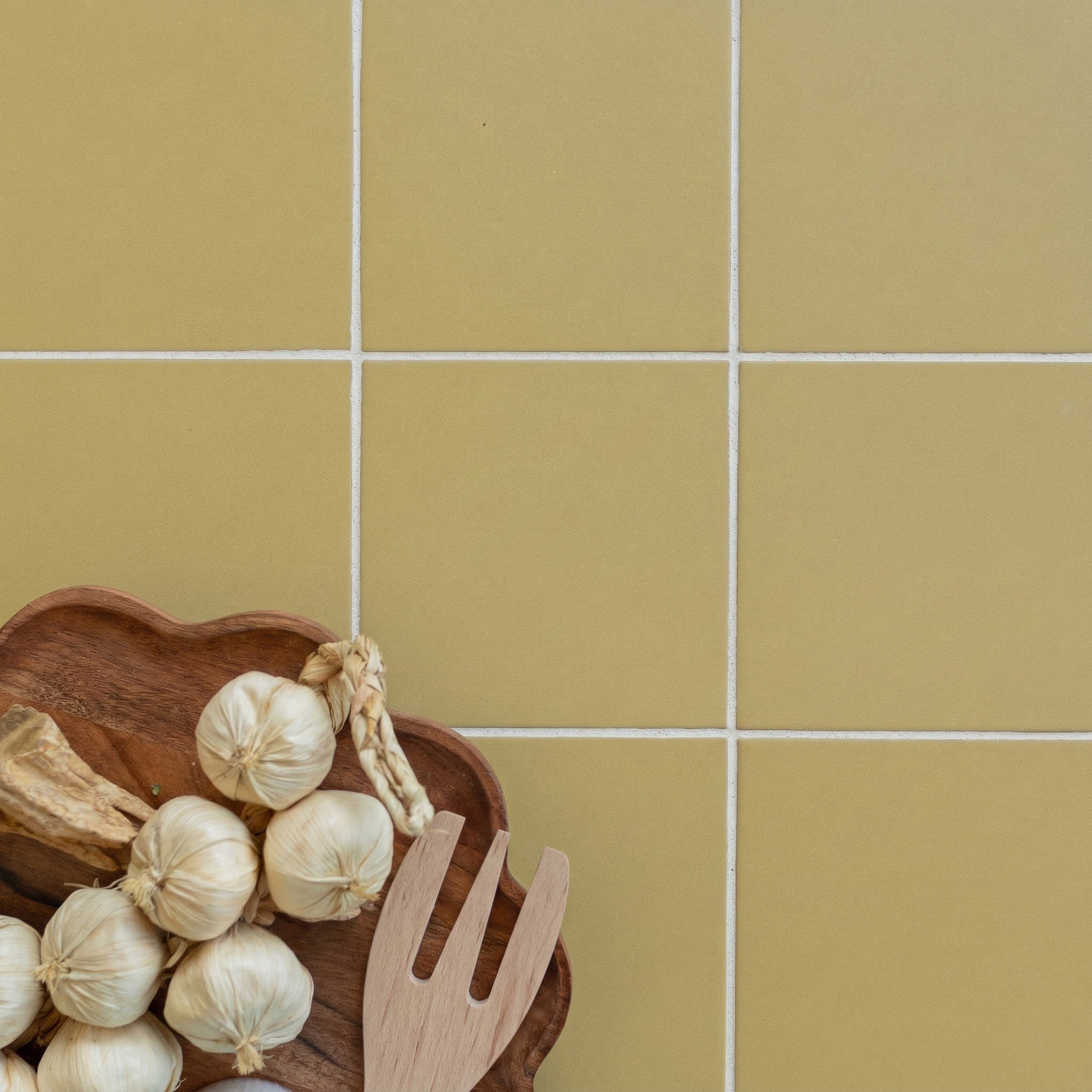 Yellow ceramic tiles with white grout and a wooden dish holding garlic bulbs and a wooden fork on the side