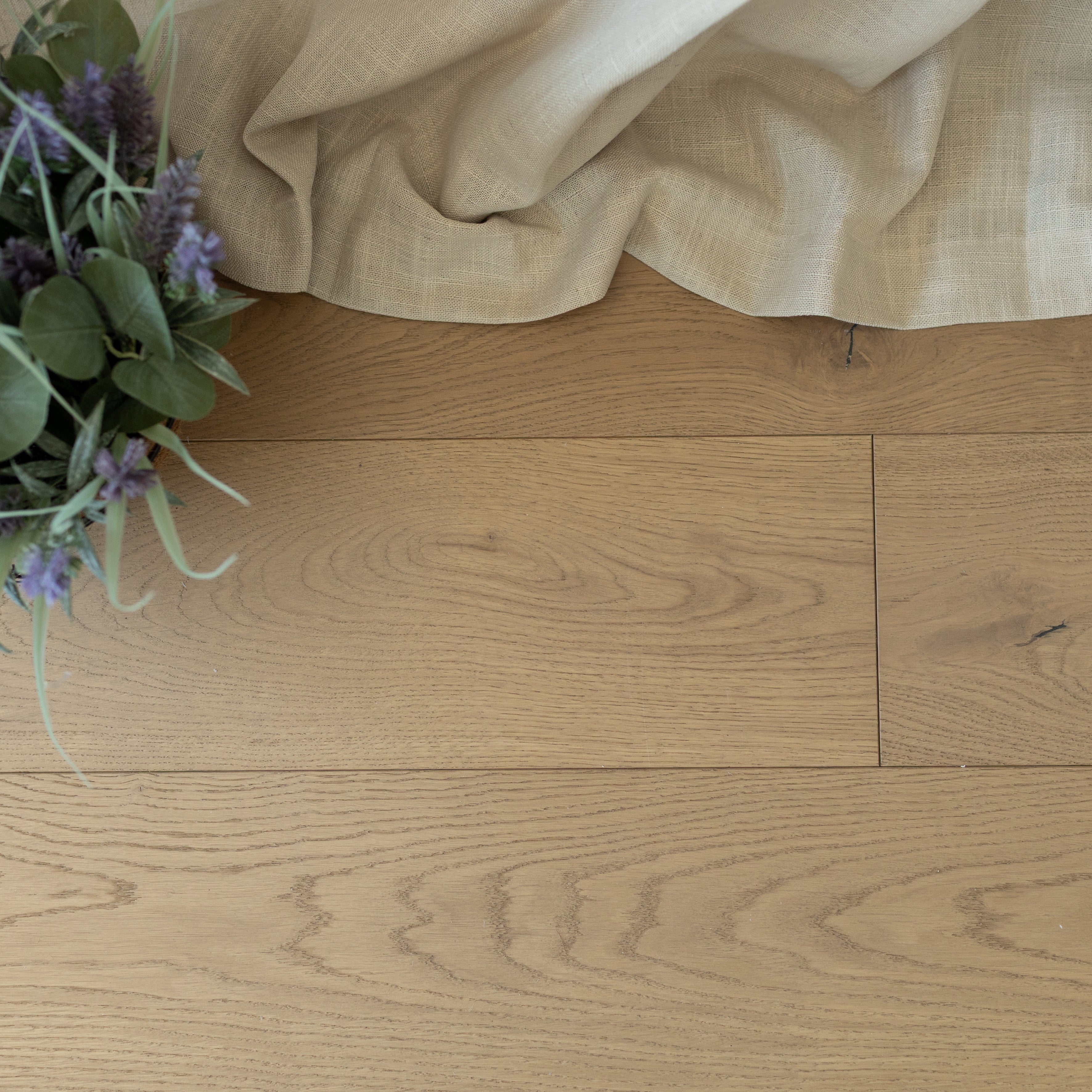 Light natural oak flooring with visible grain beneath beige linen fabric and a small potted green and purple plant detail