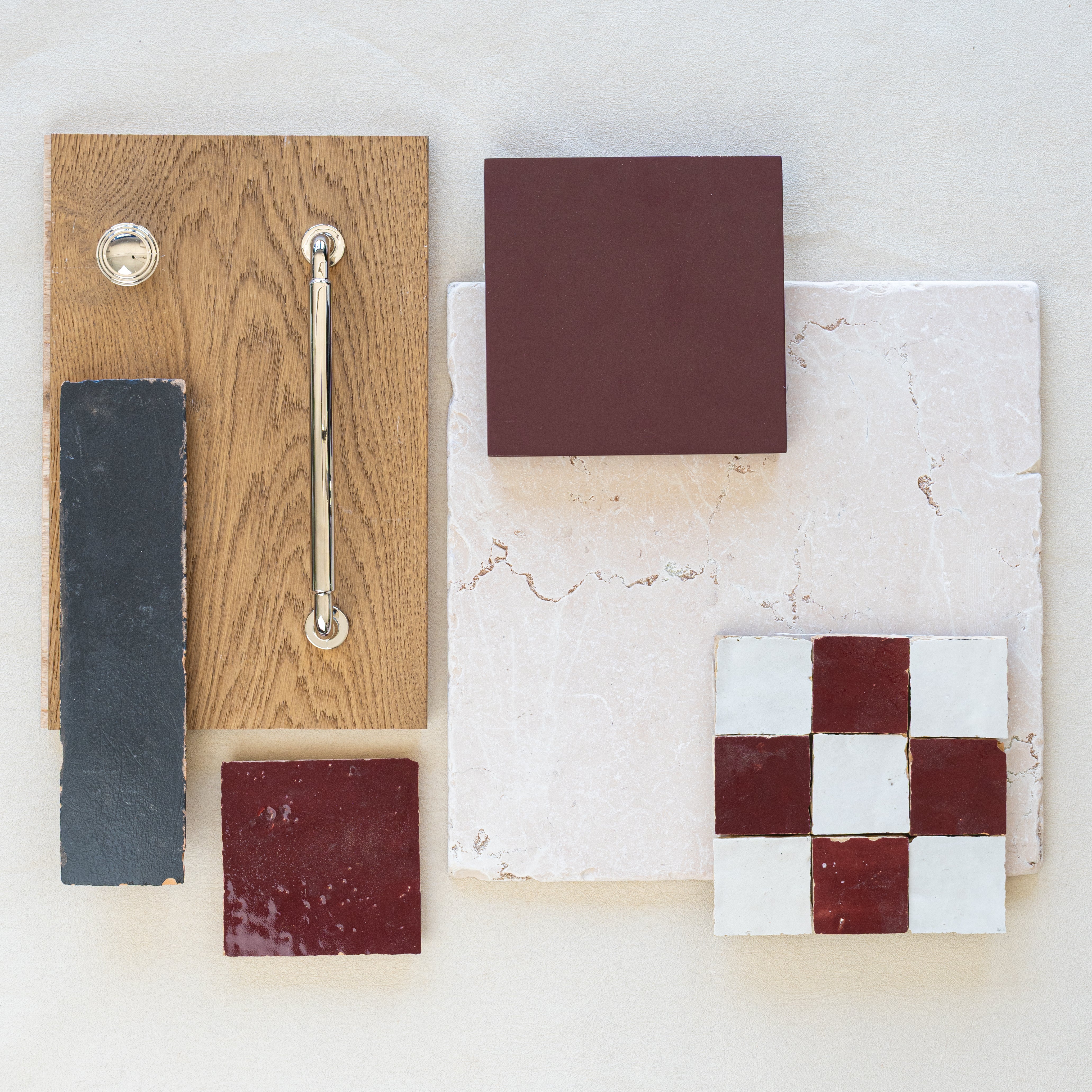 Selection of matte burgundy, glossy red and white ceramic tiles with textured beige stone and natural oak wood sample panel