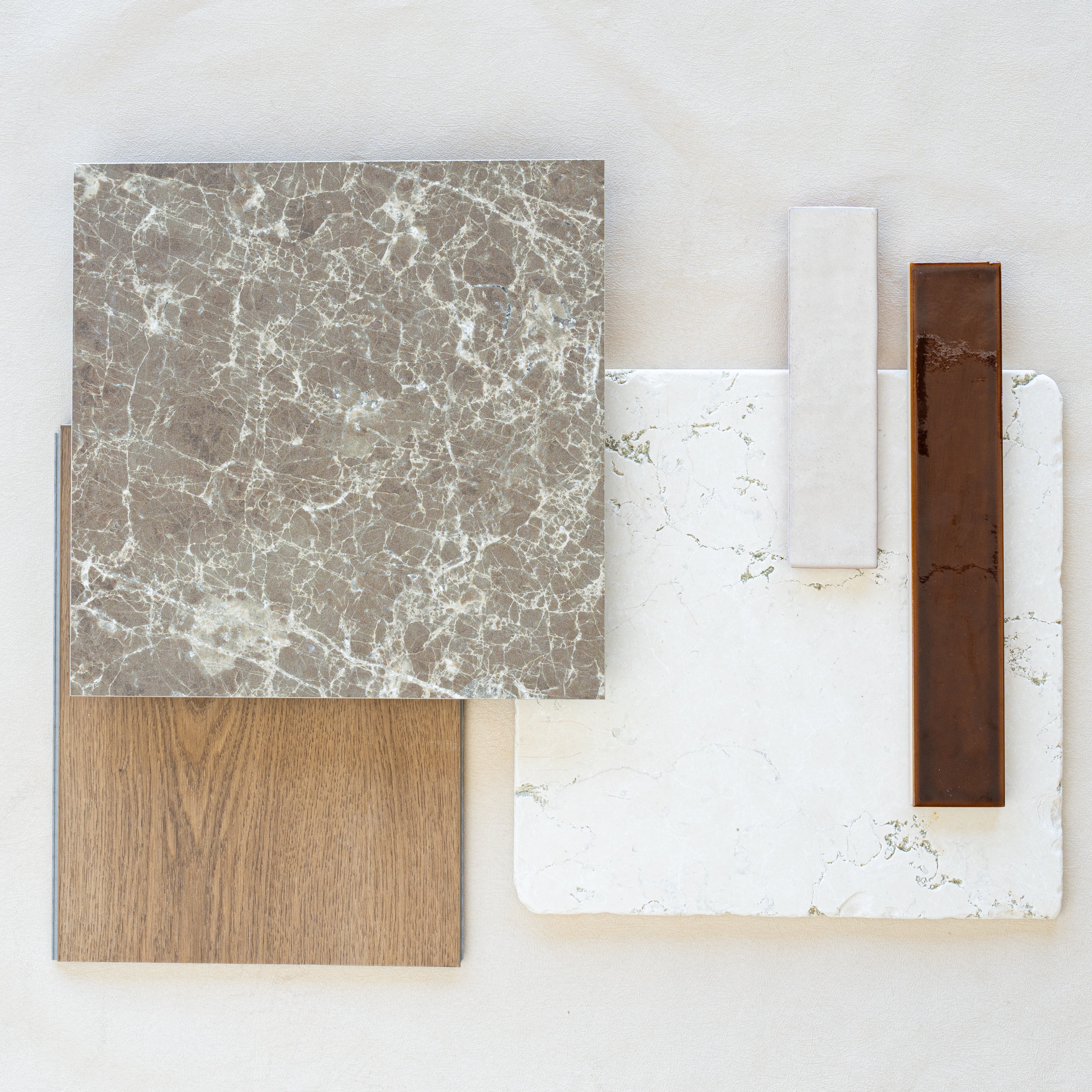 Flat lay of marble-effect tile, wood grain panel, white textured tile, and glossy brown ceramic tile samples on light surface