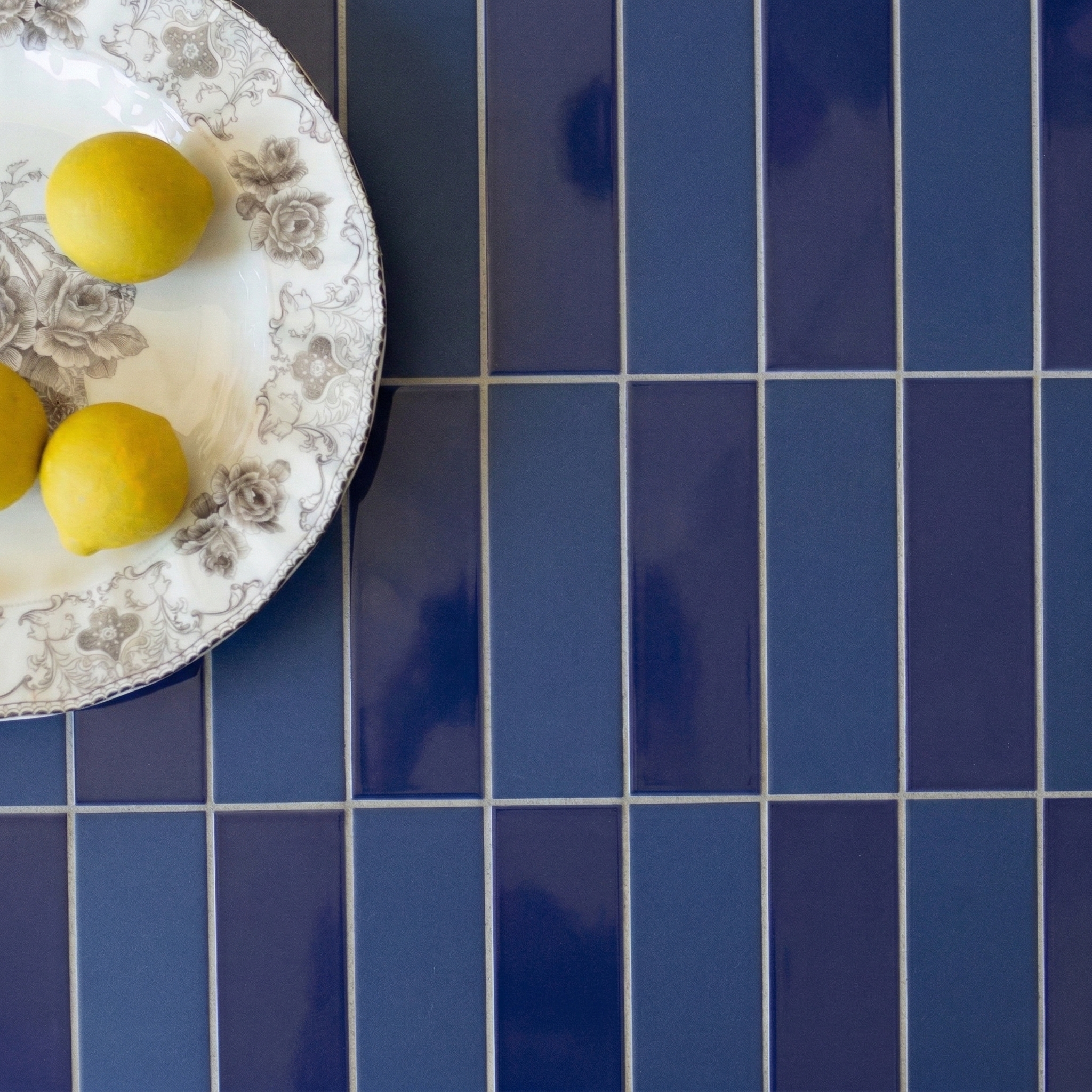 Glossy rectangular navy blue ceramic tiles with a decorative plate holding three lemons on top left corner