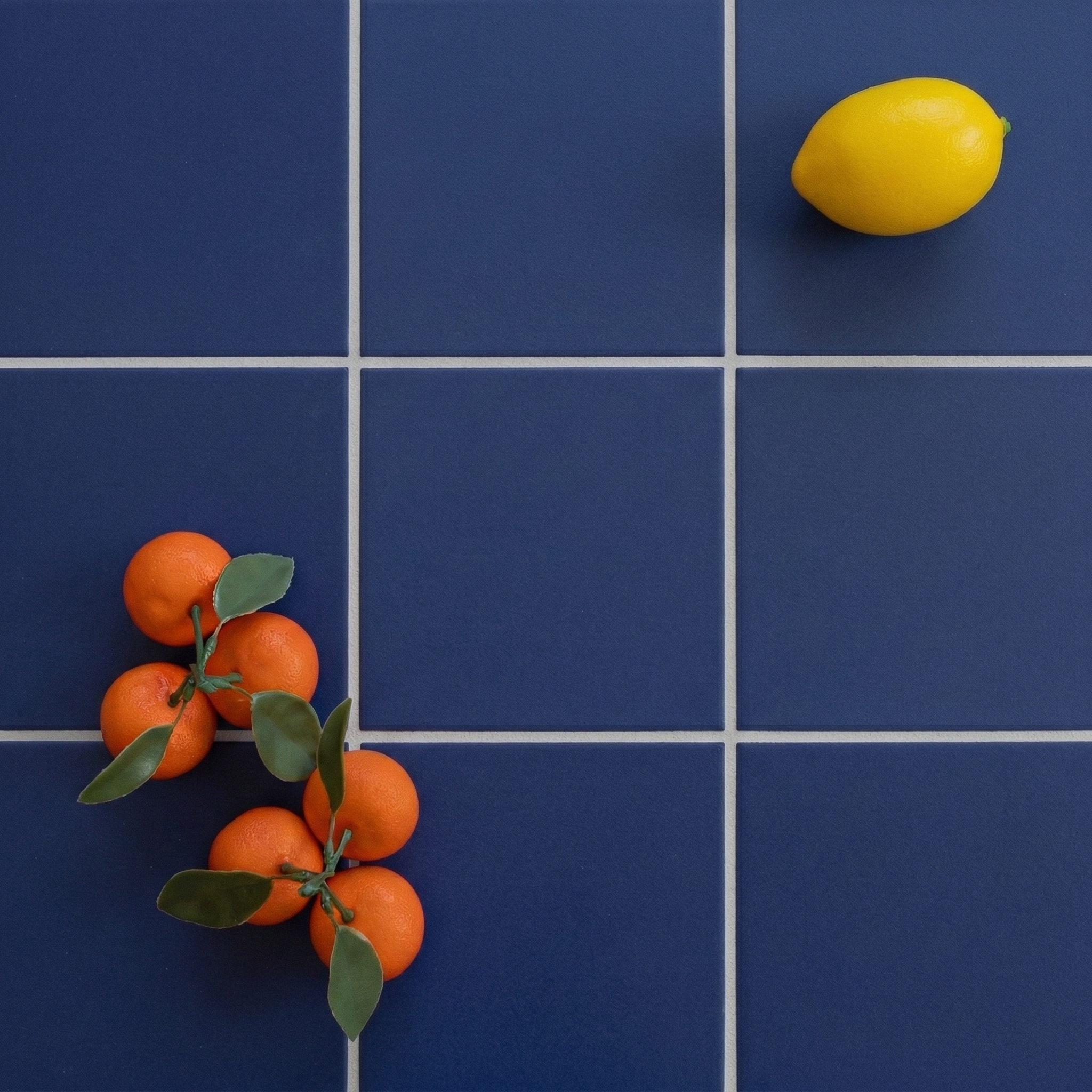 Blue ceramic tiles with white grout lines, featuring a cluster of oranges with leaves and a single lemon on top.