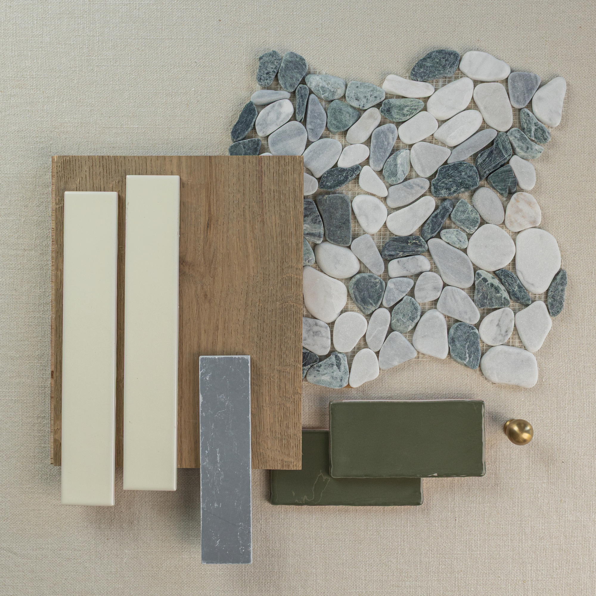 Natural stone pebbles in white and gray tones with wood plank, cream and olive tiles, and a small brass knob on fabric background