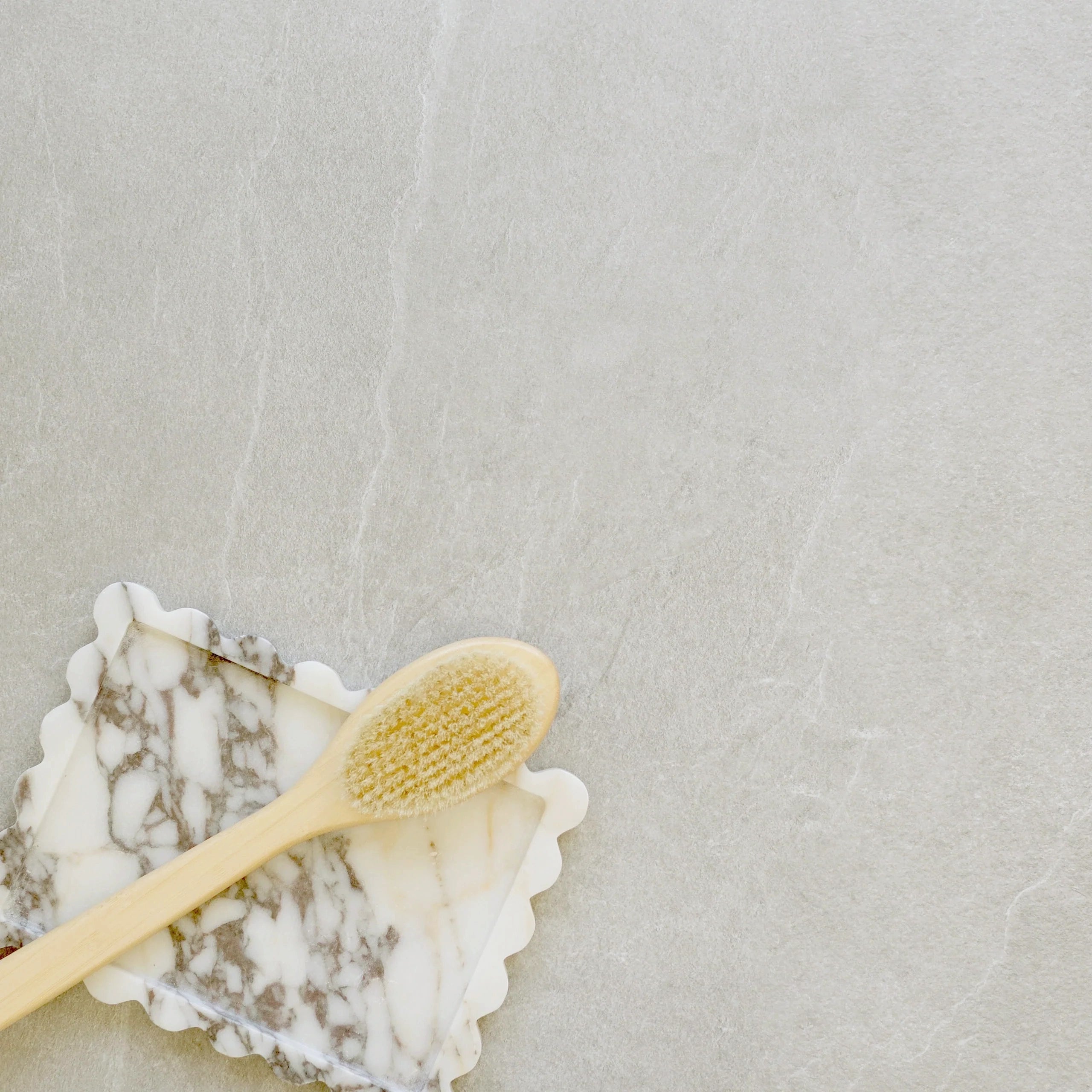 Smooth light gray porcelain tile surface with a marble soap dish and wooden bath brush resting on top