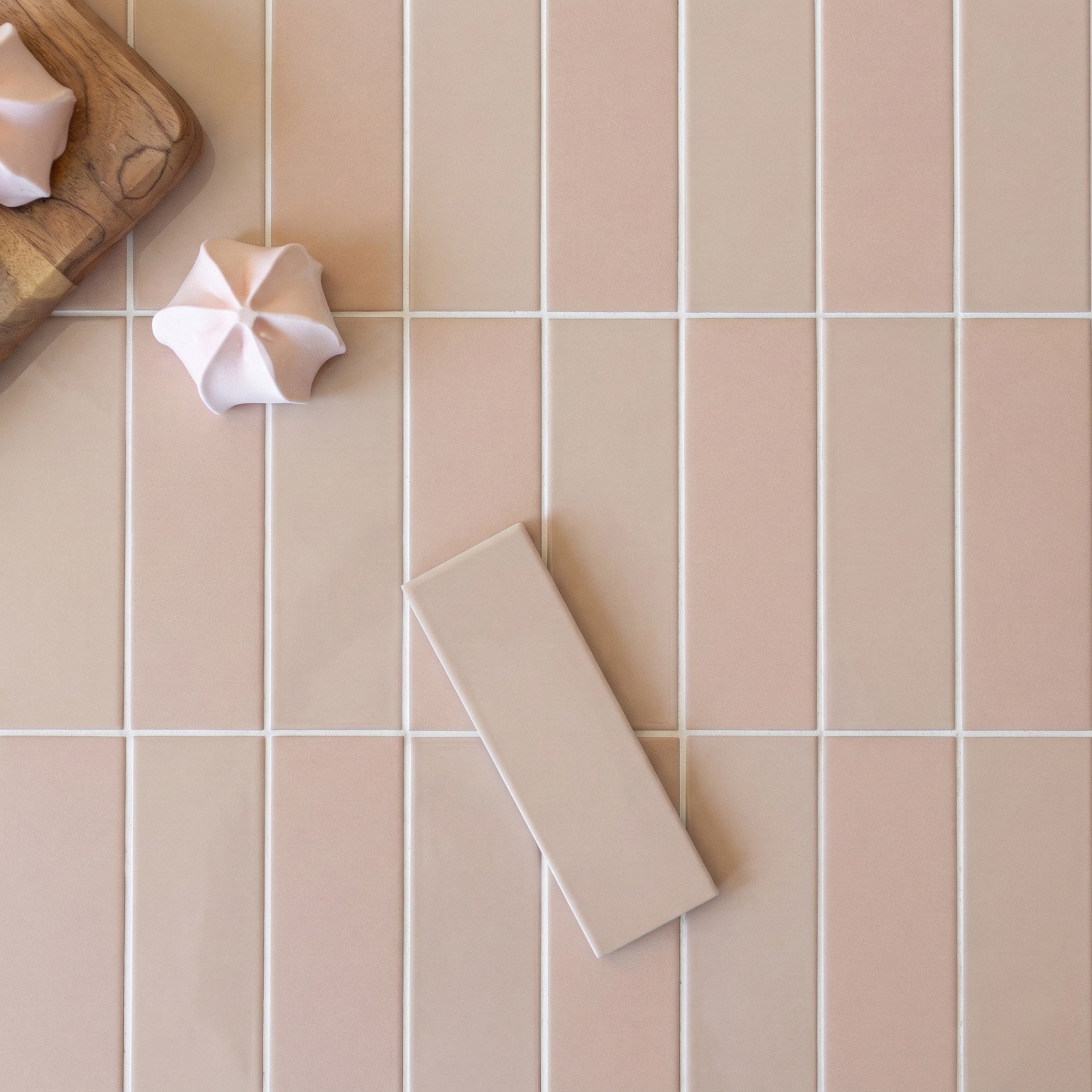 Beige rectangular porcelain tile sample on large beige vertical tile flooring with two white meringue cookies on wooden board