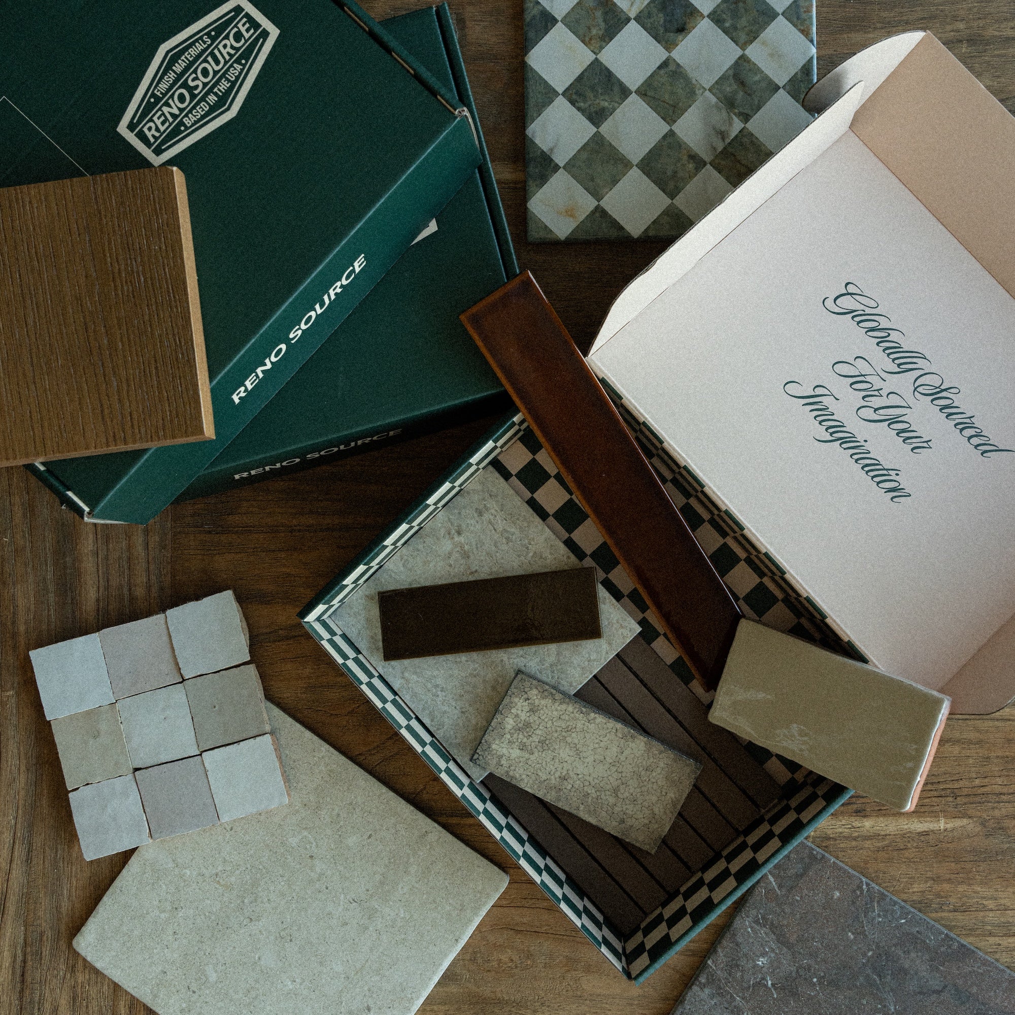 Assortment of textured tiles, wood samples, and patterned ceramics arranged near green packaging with a design motto inside a box