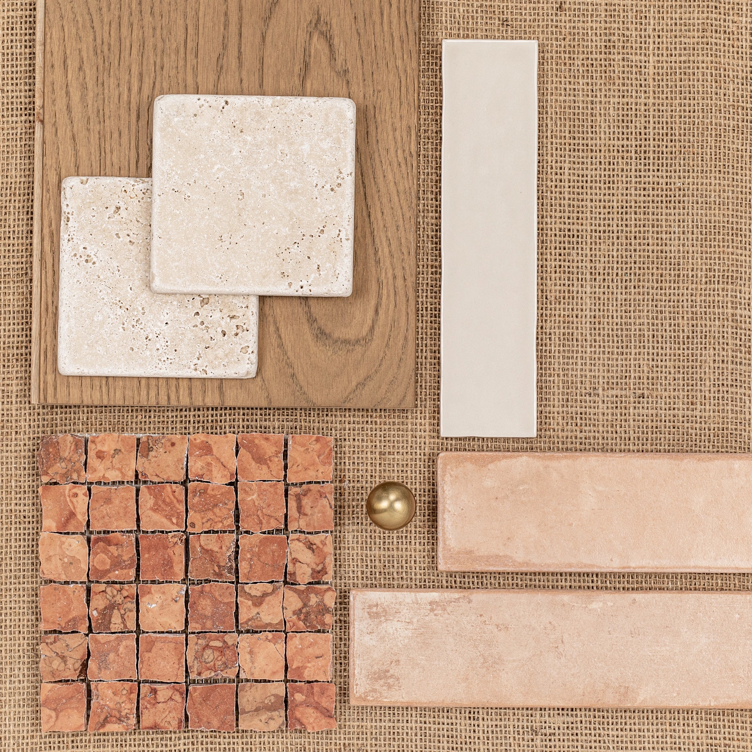 Various beige and terracotta tiles arranged on burlap and oak wood surfaces around a small brass sphere