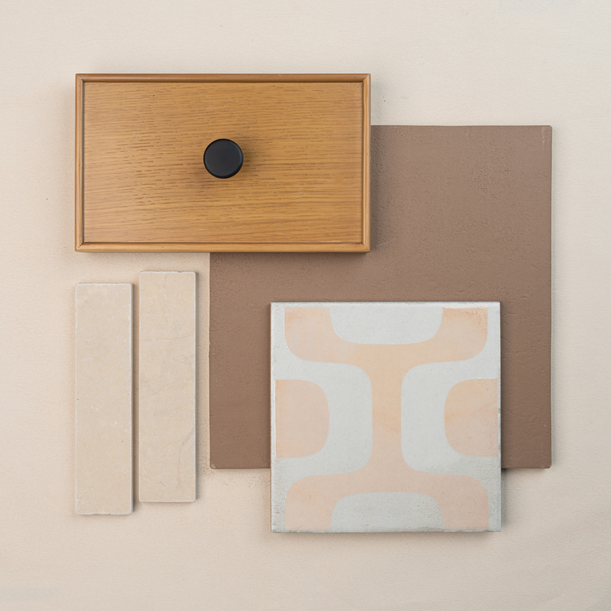 Arrangement of wood drawer front with black knob, muted brown tile, patterned ceramic tile, and two beige tile samples on neutral surface