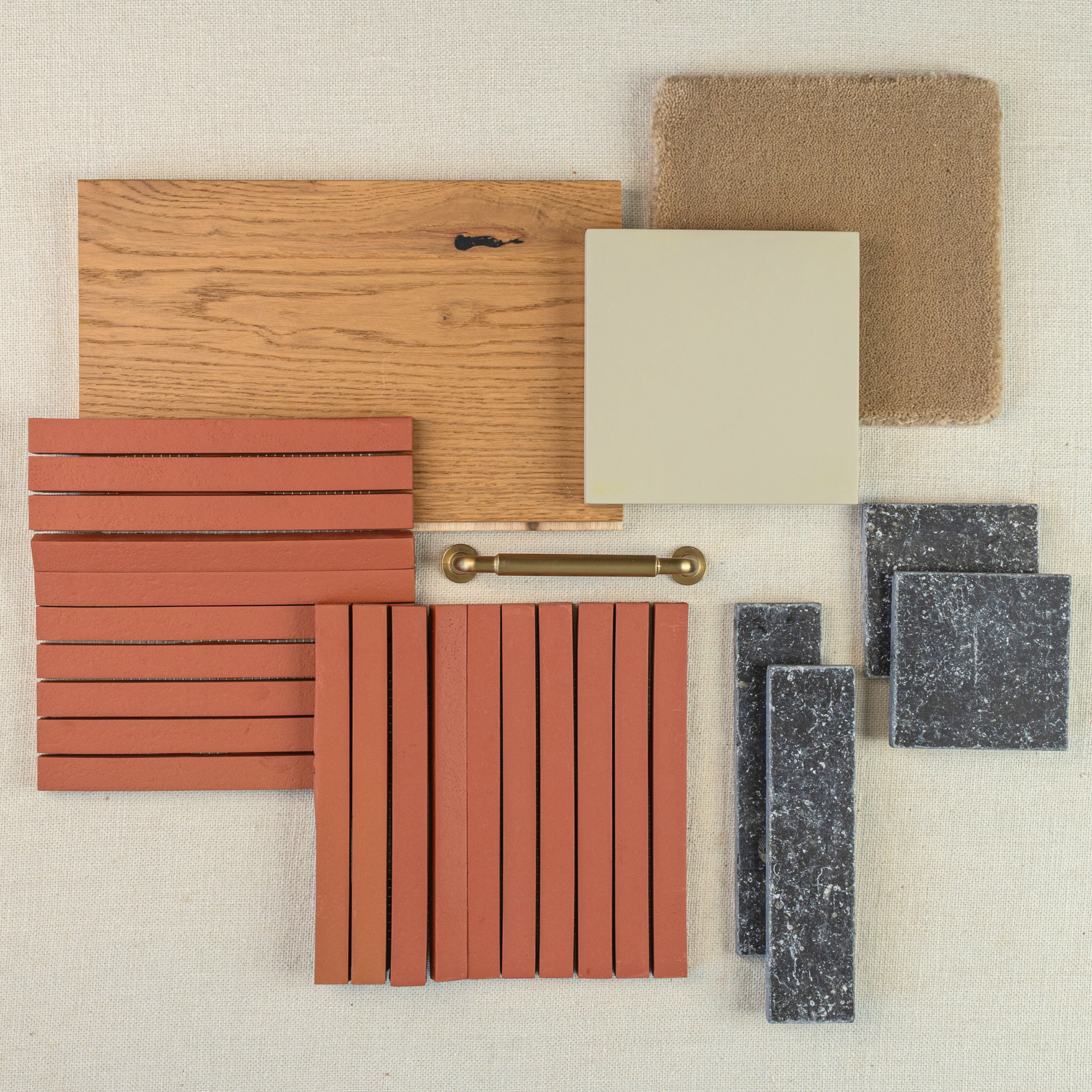 Assortment of terracotta tile strips, oak wood sample, beige ceramic square, textured fabric swatch, black stone tile, and brass handle on neutral fabric
